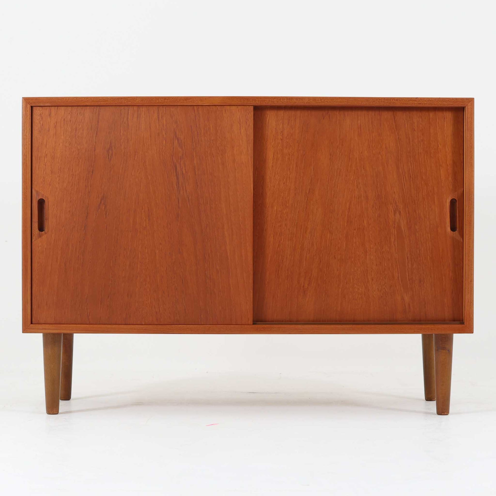 デンマーク製ボードです。チーク材のあたたかみある木肌を前面に活かし、側板や脚部にビーチ材を組み合わせた軽やかな佇まいが魅力。すっきりとした引き戸と細身の丸脚により、小ぶりながら北欧らしい洗練された存在感を備えています。内部は左右に棚板を備え、食器や書類、リビング小物をすっきり収納可能。天板には照明やオブジェを飾りやすく、サイドボードやテレビボード、玄関収納としても取り入れやすいサイズ感です。経年で深みを増した木色と丁寧な造りが、ビンテージならではの上質さを空間に添える一品です。