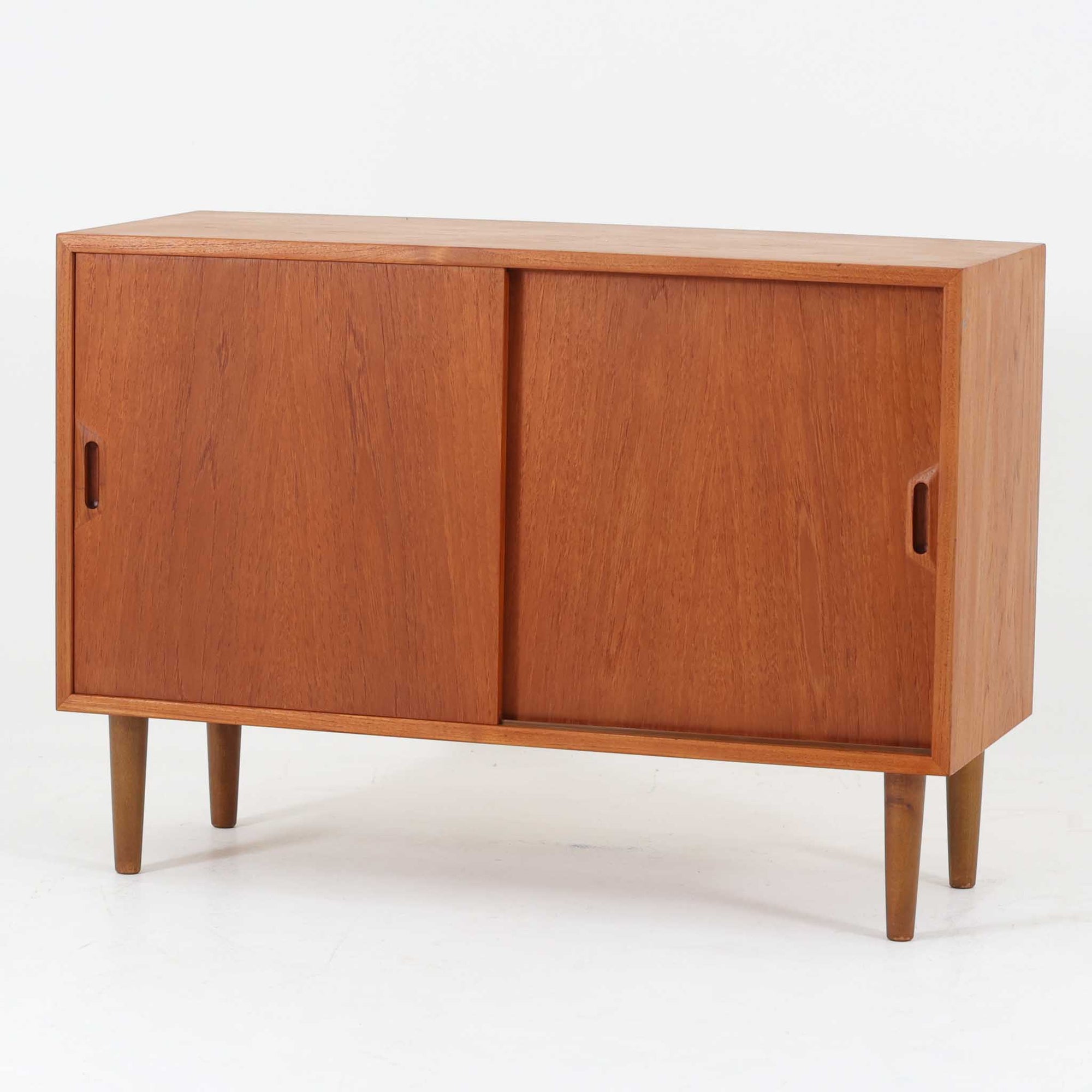 デンマーク製ボードです。チーク材のあたたかみある木肌を前面に活かし、側板や脚部にビーチ材を組み合わせた軽やかな佇まいが魅力。すっきりとした引き戸と細身の丸脚により、小ぶりながら北欧らしい洗練された存在感を備えています。内部は左右に棚板を備え、食器や書類、リビング小物をすっきり収納可能。天板には照明やオブジェを飾りやすく、サイドボードやテレビボード、玄関収納としても取り入れやすいサイズ感です。経年で深みを増した木色と丁寧な造りが、ビンテージならではの上質さを空間に添える一品です。