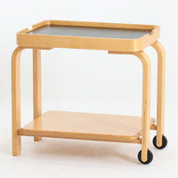 Carina Bengsがデザインし、IKEAで製作された「Brunabo」シリーズのキャスターワゴンです。バーチ材を使用した明るくやわらかな木目が特徴で、北欧らしいシンプルで温かみのあるデザインに仕上げられています。2000年代に製作されたモデルで、現在はすでに生産終了していると考えられ、ビンテージとして楽しめるアイテムです。上段は取り外し可能なトレイ仕様になっており、飲み物や小物を運ぶサービングトレイとしても使用できる実用的な構造。トレイを外した状態でも天板として使えるため、用途に応じた使い方が可能です。下段には棚板が設けられており、雑誌やキッチン用品、日用品などを収納できます。また片側のみにキャスターが付いた設計になっているため、一般的なワゴンよりも安定感があり、必要な時だけ持ち上げて移動できる使い勝手の良さも魅力。リビングやダイニング、キッチンなどさまざまな空間で活躍する、北欧らしい機能性とデザイン性を兼ね備えたワゴンです。