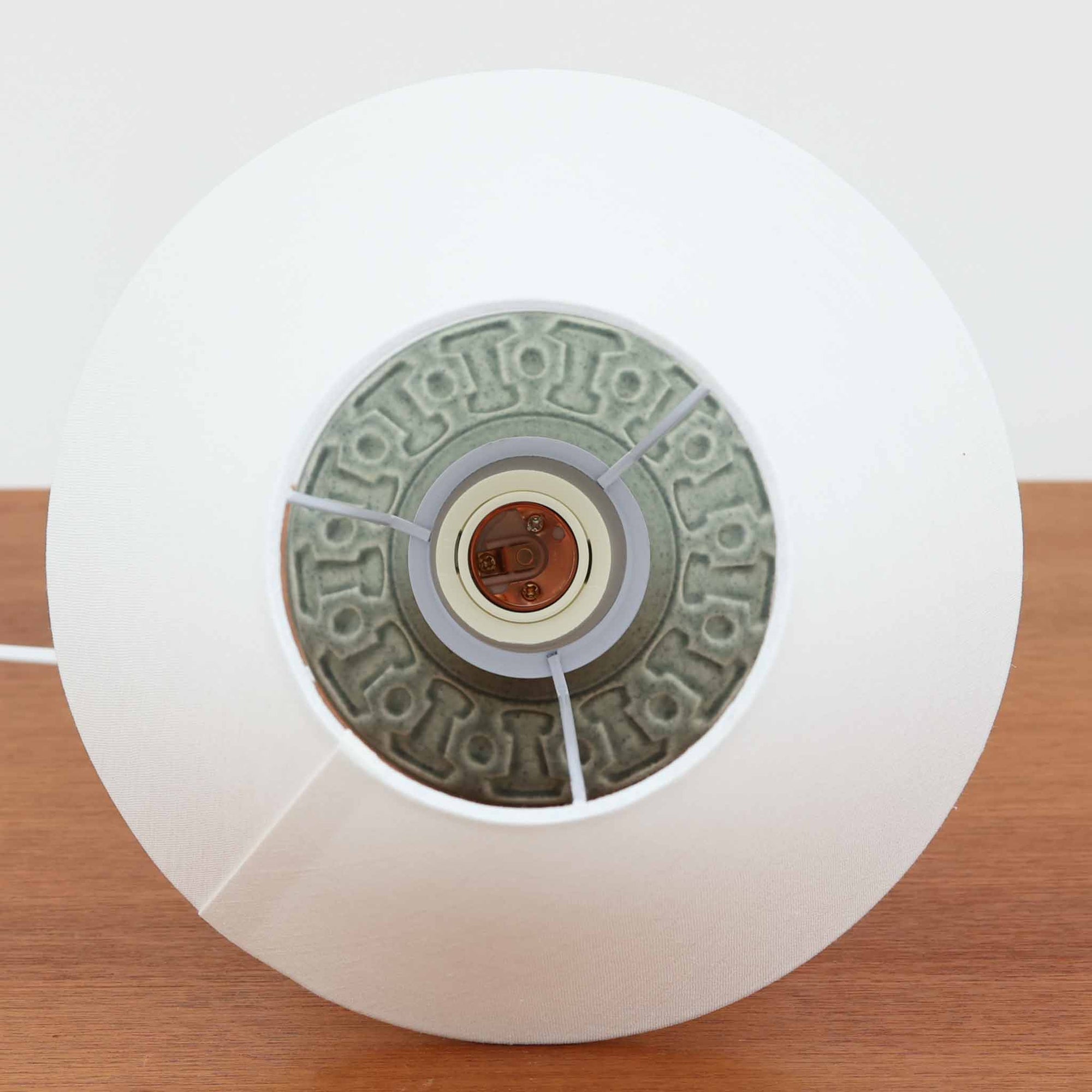 Einar Johansenがデザインし、Soholm Keramikが製作したモデル1028のテーブルランプです。高さ33cmの使いやすいサイズに、淡いセージグリーンの陶磁器ベースと上質なリネンシェードを組み合わせた、北欧らしい静かな佇まいが魅力。胴部にぐるりと施された幾何学的なレリーフ文様が美しい陰影を生み、点灯時にはやわらかな光とともに立体感がより際立ちます。チェストやサイドテーブル、ベッドサイドにも馴染みやすく、落ち着いた色調が空間にやさしい温もりを添える一台。Johansenならではの端正な造形とSoholmの高い陶芸技術を感じられる、希少性の高いビンテージ照明です。