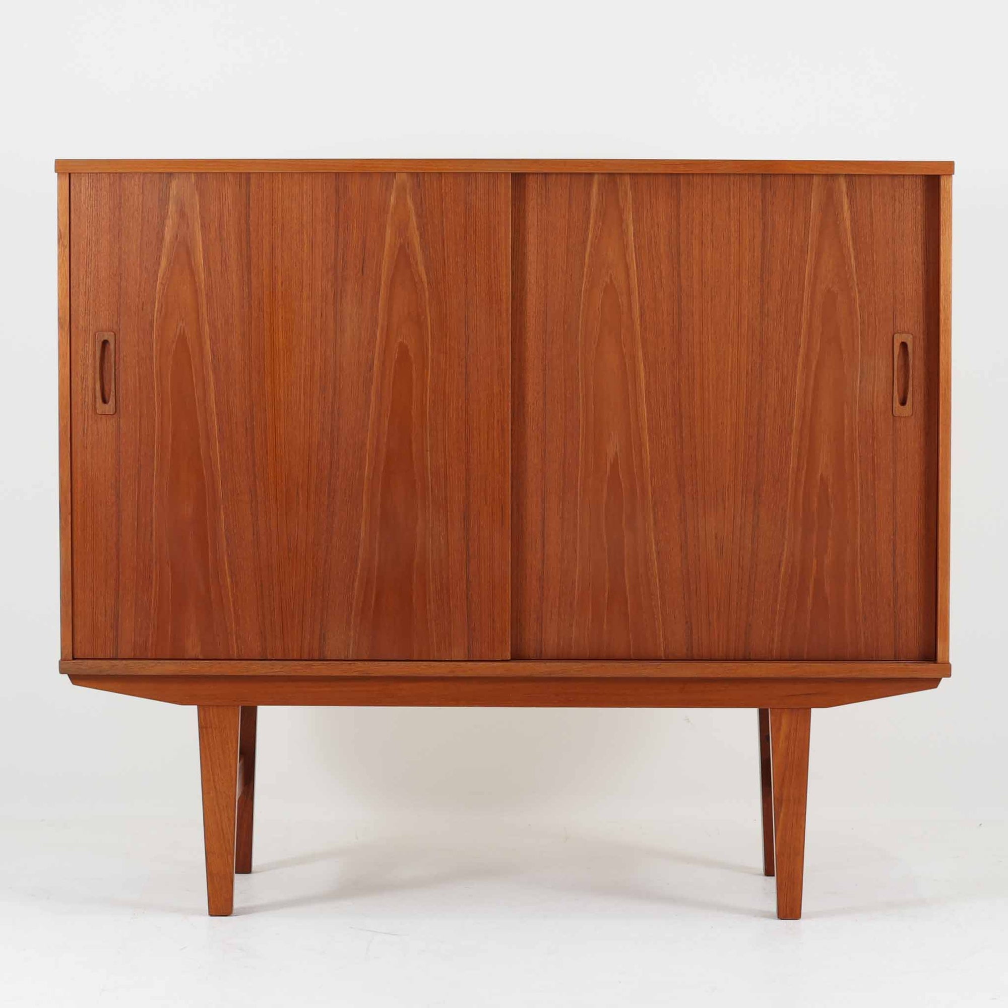 良質な木材を使用した本体は、美しい木目と経年により深みを増した色艶が魅力で、空間に落ち着いた存在感をもたらします。コンパクトなサイズ感ながら、引き戸内部には可動棚やトレイ収納を備え、食器や書類、小物を機能的に整理できる実用的な設計。すっきりとしたフォルムに対し、わずかに外側へ広がる脚部が軽やかさと安定感を両立し、ビンテージならではの丁寧な作りと佇まいを感じさせます。リビングやダイニングの収納家具としてはもちろん、ディスプレイ台としても活躍する一台です。