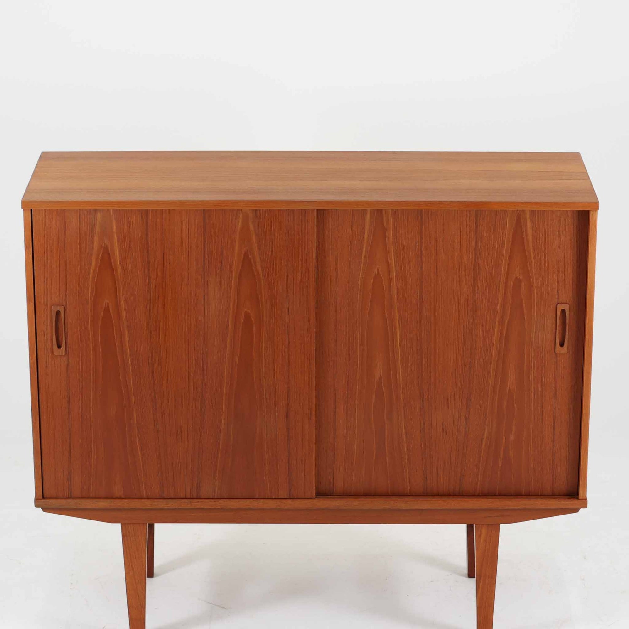 良質な木材を使用した本体は、美しい木目と経年により深みを増した色艶が魅力で、空間に落ち着いた存在感をもたらします。コンパクトなサイズ感ながら、引き戸内部には可動棚やトレイ収納を備え、食器や書類、小物を機能的に整理できる実用的な設計。すっきりとしたフォルムに対し、わずかに外側へ広がる脚部が軽やかさと安定感を両立し、ビンテージならではの丁寧な作りと佇まいを感じさせます。リビングやダイニングの収納家具としてはもちろん、ディスプレイ台としても活躍する一台です。