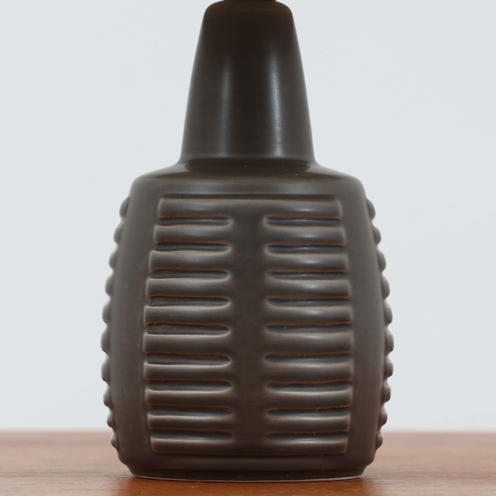 Rigmor Nielsenがデザインし、Soholm Keramikが手掛けたテーブルランプです。高さ37cmの取り入れやすいサイズに、艶やかな陶磁器ベースとナチュラルなリネンシェードを組み合わせた、落ち着きある北欧ビンテージらしい一台。ベースには規則的な立体リブ装飾が施され、陰影豊かな表情と彫刻的な存在感を生み出しています。点灯時にはシェード越しの柔らかな光が釉薬の奥行きや貫入の表情を引き立て、チェストやサイドテーブル、ベッドサイドに穏やかな雰囲気を演出。Rigmor Nielsenらしい造形美とSoholmの高い陶芸技術が感じられる、希少性の高いビンテージ照明です。