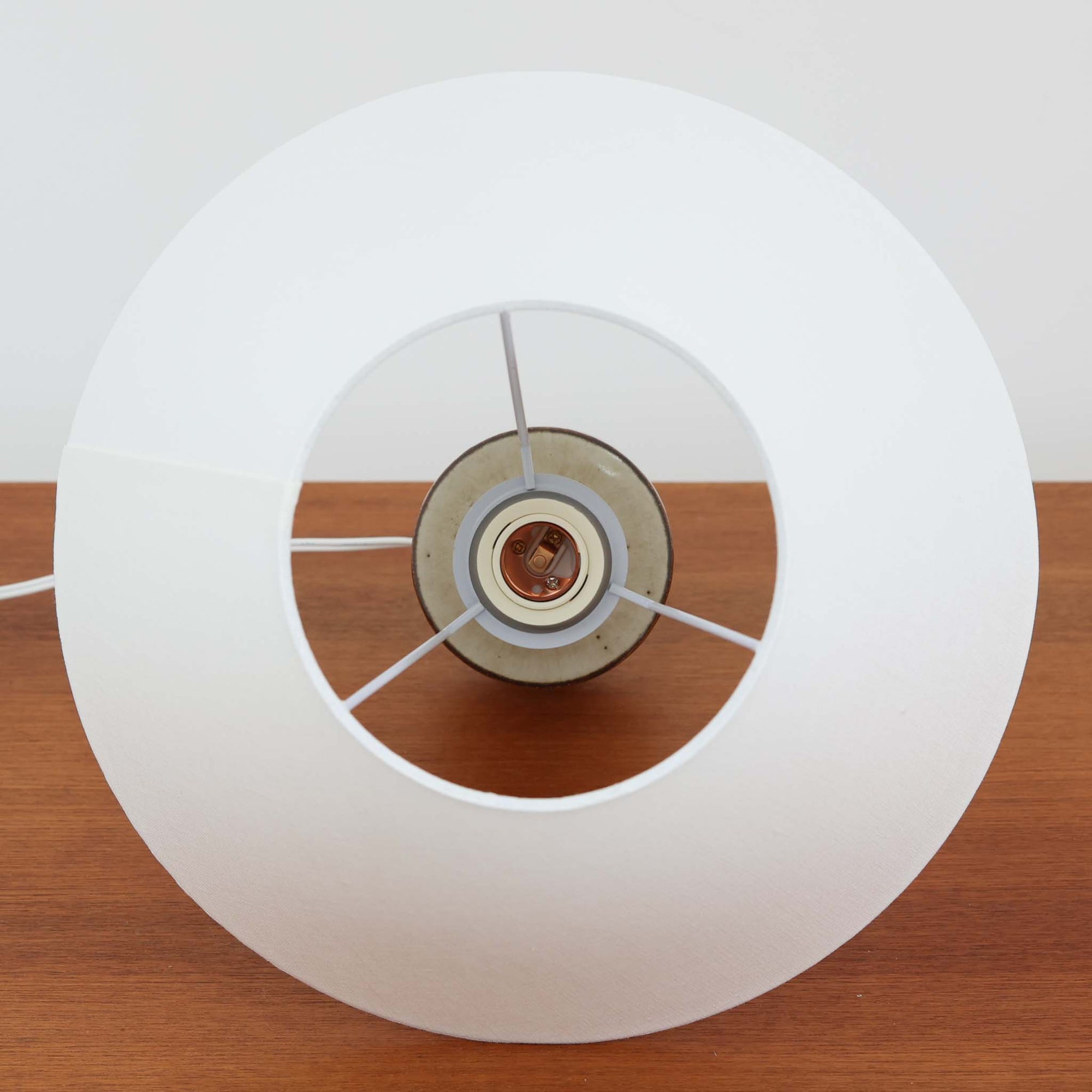 Joseph Simonデザイン、Soholm Keramik製モデル3059のデンマーク製テーブルランプです。陶磁器ベースは、やわらかなアイボリーを基調にブラウンが層状に溶け合う美しい流釉が印象的で、くびれを効かせた縦長フォルムに段差を設けた造形がミッドセンチュリーらしい端正さを感じさせます。釉薬の自然な濃淡と細かな鉄点が一点ごとに異なる豊かな表情を生み、灯りを点すとリネンシェード越しの柔らかな光が陶肌の温もりをより引き立てます。サイドテーブルやチェスト、ベッドサイドの間接照明として使いやすい高さ44cmで、北欧ビンテージならではの職人技と経年の味わいを楽しめるコレクタブルな一台です。