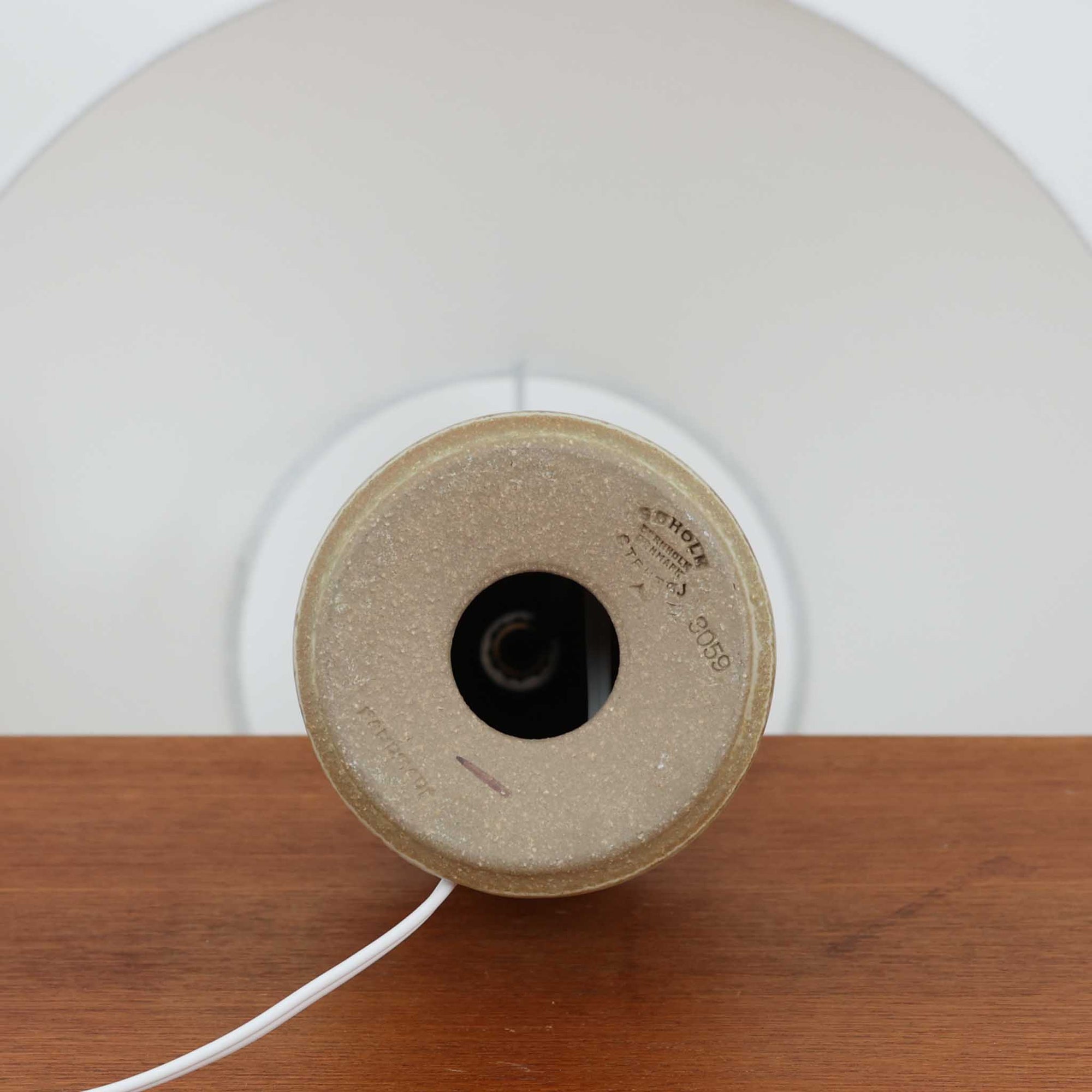 Joseph Simonデザイン、Soholm Keramik製モデル3059のデンマーク製テーブルランプです。陶磁器ベースは、やわらかなアイボリーを基調にブラウンが層状に溶け合う美しい流釉が印象的で、くびれを効かせた縦長フォルムに段差を設けた造形がミッドセンチュリーらしい端正さを感じさせます。釉薬の自然な濃淡と細かな鉄点が一点ごとに異なる豊かな表情を生み、灯りを点すとリネンシェード越しの柔らかな光が陶肌の温もりをより引き立てます。サイドテーブルやチェスト、ベッドサイドの間接照明として使いやすい高さ44cmで、北欧ビンテージならではの職人技と経年の味わいを楽しめるコレクタブルな一台です。
