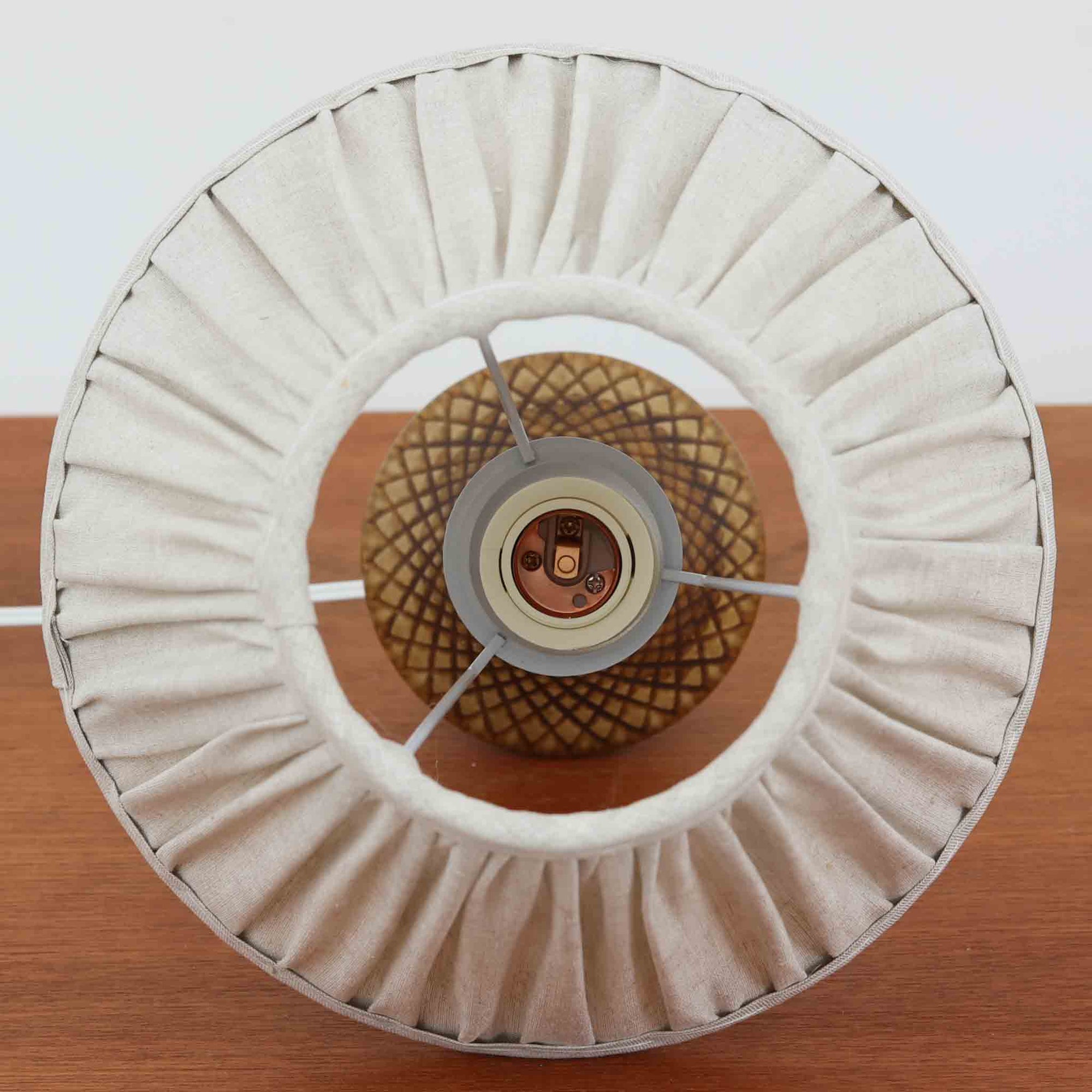 Einar Johansenデザイン、Soholm Keramik製モデル926のデンマーク製テーブルランプです。あたたかなキャメルブラウンの陶磁器ベースに、菱形が連続する繊細なハンドカット風の幾何学模様と、首元のシャープな三角装飾が美しく映える一台。裾へ広がる低重心フォルムとすっと伸びるネックの対比が印象的で、エイナー・ヨハンセンらしい洗練された造形美を感じさせます。プリーツ状のリネンシェードからこぼれる柔らかな灯りが模様の陰影を豊かに引き立て、ベッドサイドやサイドチェスト、飾り棚のアクセント照明として空間に上品な温もりを添えます。経年で深みを増した釉薬の艶と希少なデザイナーズモデルならではの存在感を楽しめる北欧ビンテージらしい逸品です。