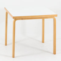 Alvar Aaltoがデザインし、Artekが製作したモデル81Cの正方形ダイニングテーブルです。バーチ材のしなやかな曲木脚とホワイトラミネート天板の組み合わせが、アアルトらしい機能美と軽やかな佇まいを生み出しています。幅75cmの扱いやすいサイズは2人用のダイニングテーブルとしてはもちろん、ワークデスクやショップ什器としても取り入れやすい一台。経年により深みを増した木肌と、長年使い込まれた天板の風合いがビンテージならではの味わいを感じさせ、Artekの普遍的なデザイン性と希少な北欧オリジナルの存在感を空間に添えてくれます。