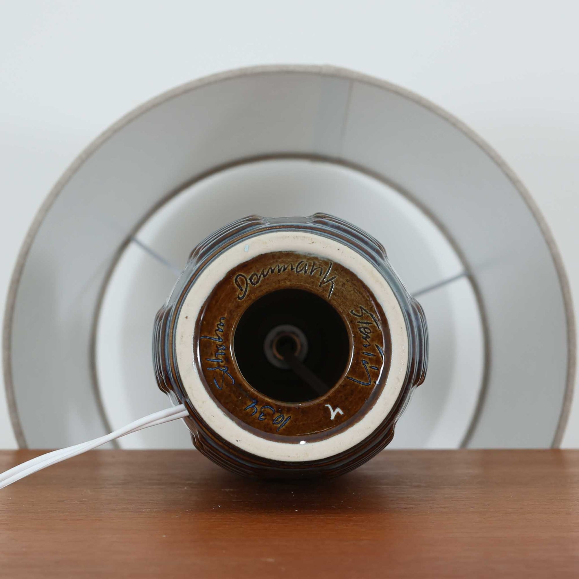 Soholm Keramikのモデル1034、Einar Johansenデザインによるデンマーク製ビンテージテーブルランプです。縦に伸びる端正なフォルムに、規則的に刻まれた立体的なレリーフが陰影を生み、深みのあるブルーの釉薬が豊かな表情を引き立てています。エイナー・ヨハンセンらしい彫刻的な造形美と、スーホルムならではの美しい焼成技術が融合した存在感のある一台。リネンシェードからこぼれる柔らかな灯りが陶器の陰影をより際立たせ、サイドボードやチェスト、ベッドサイドのアクセント照明として空間に上質な北欧らしさを添えてくれます。希少なモデルならではのコレクション性も魅力です。