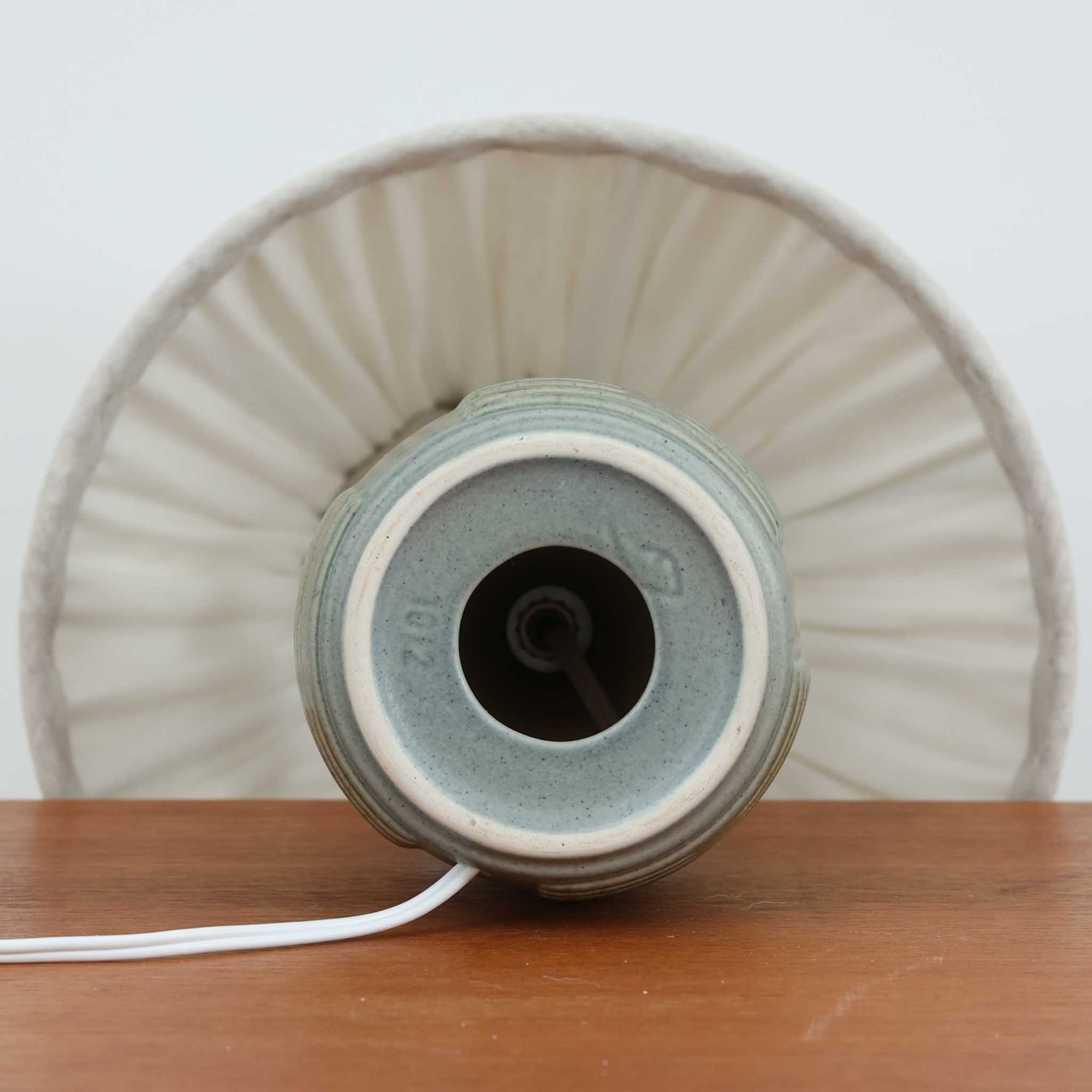 Einar Johansenがデザインし、Soholm Keramikが手掛けたテーブルランプです。高さ37cmの取り入れやすいサイズに、艶やかな陶磁器ベースとナチュラルなリネンシェードを組み合わせた、落ち着きある北欧ビンテージらしい一台。ベースには規則的な立体リブ装飾が施され、陰影豊かな表情と彫刻的な存在感を生み出しています。点灯時にはシェード越しの柔らかな光が釉薬の奥行きや貫入の表情を引き立て、チェストやサイドテーブル、ベッドサイドに穏やかな雰囲気を演出。Einar Johansenらしい造形美とSoholmの高い陶芸技術が感じられる、希少性の高いビンテージ照明です。