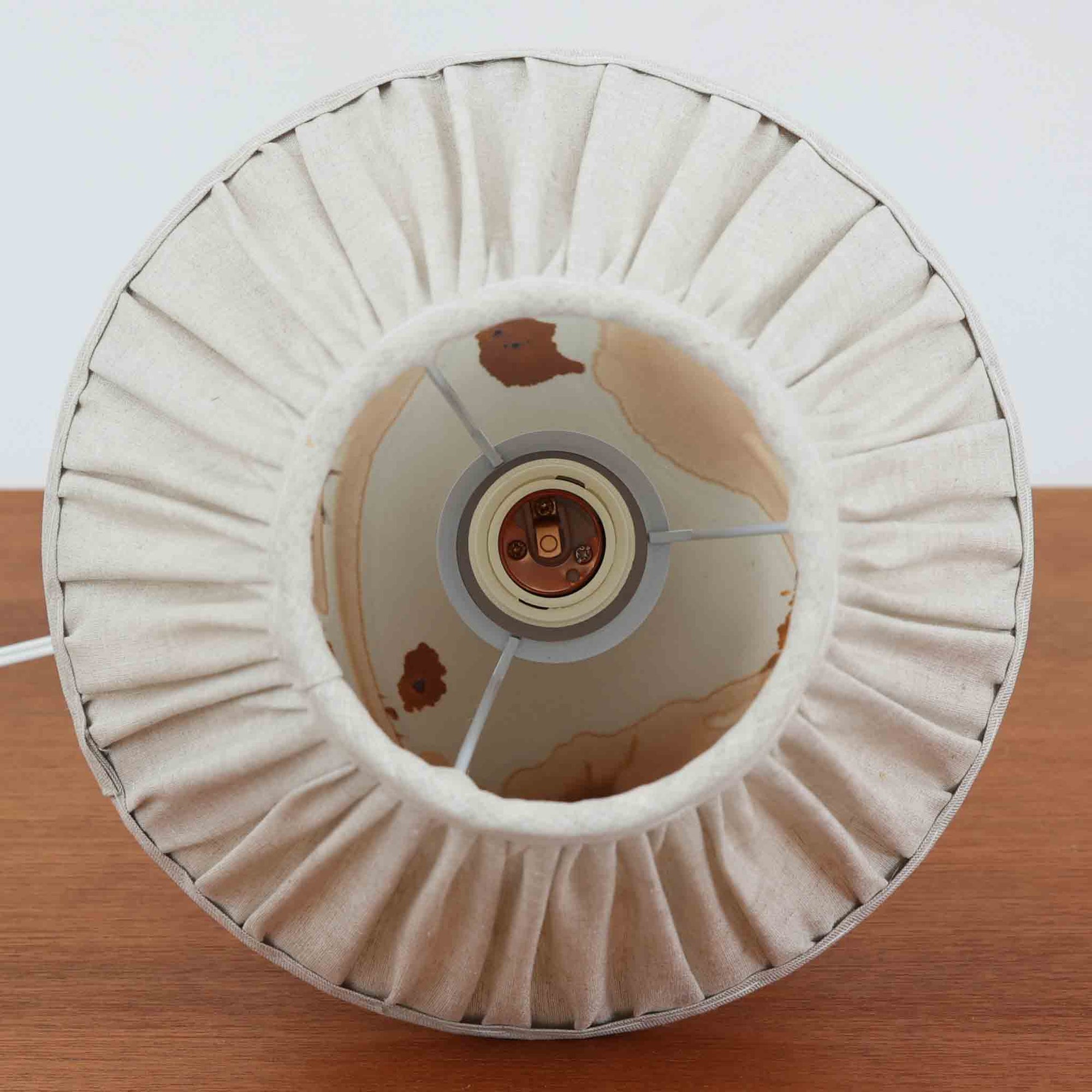 Soholm Keramikのモデル3063-2、Noomi Backhausenデザインによるデンマーク製ビンテージテーブルランプです。丸みを帯びた愛らしい陶磁器ベースに、ノーミ・バックハウゼンらしい抽象的で有機的なブラウンの流線模様が描かれ、柔らかなアイボリー地とのコントラストが温かみある表情を生み出しています。手仕事ならではの偶然性を感じる釉薬のにじみや濃淡が一点ごとの個性を際立たせる魅力的なモデル。プリーツシェードからこぼれるやさしい灯りが、ベッドサイドやチェスト上を穏やかに照らし、北欧らしいやわらかな空気感を添えてくれます。小ぶりながら存在感があり、コレクション性も高い一台です。
