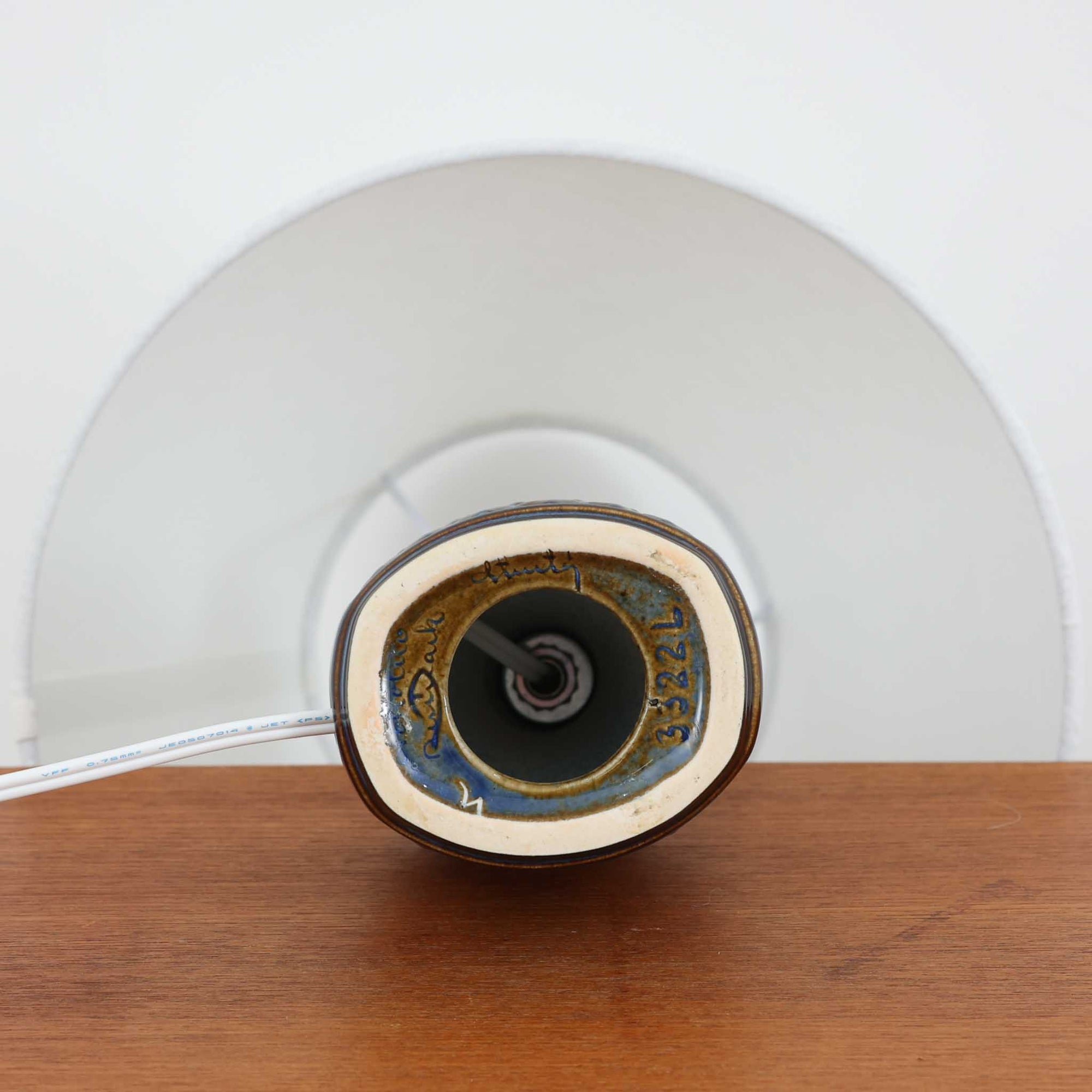 Soholm Keramikのモデル3322L、Einar Johansenデザインによるデンマーク製ビンテージテーブルランプです。コンパクトな陶磁器ベースに、幾何学的に連なる立体レリーフが美しい陰影を生み、深いネイビーブルーの釉薬が落ち着きと品格を添えています。エイナー・ヨハンセンらしい建築的な意匠と、スーホルムならではの艶やかな焼成技術が融合した小ぶりながら存在感のある一台。リネンシェードから広がる柔らかな灯りが立体模様をより引き立て、ベッドサイドやチェスト、飾り棚のアクセント照明として空間に北欧らしい洗練をもたらします。希少なモデルならではのコレクション性も魅力です。