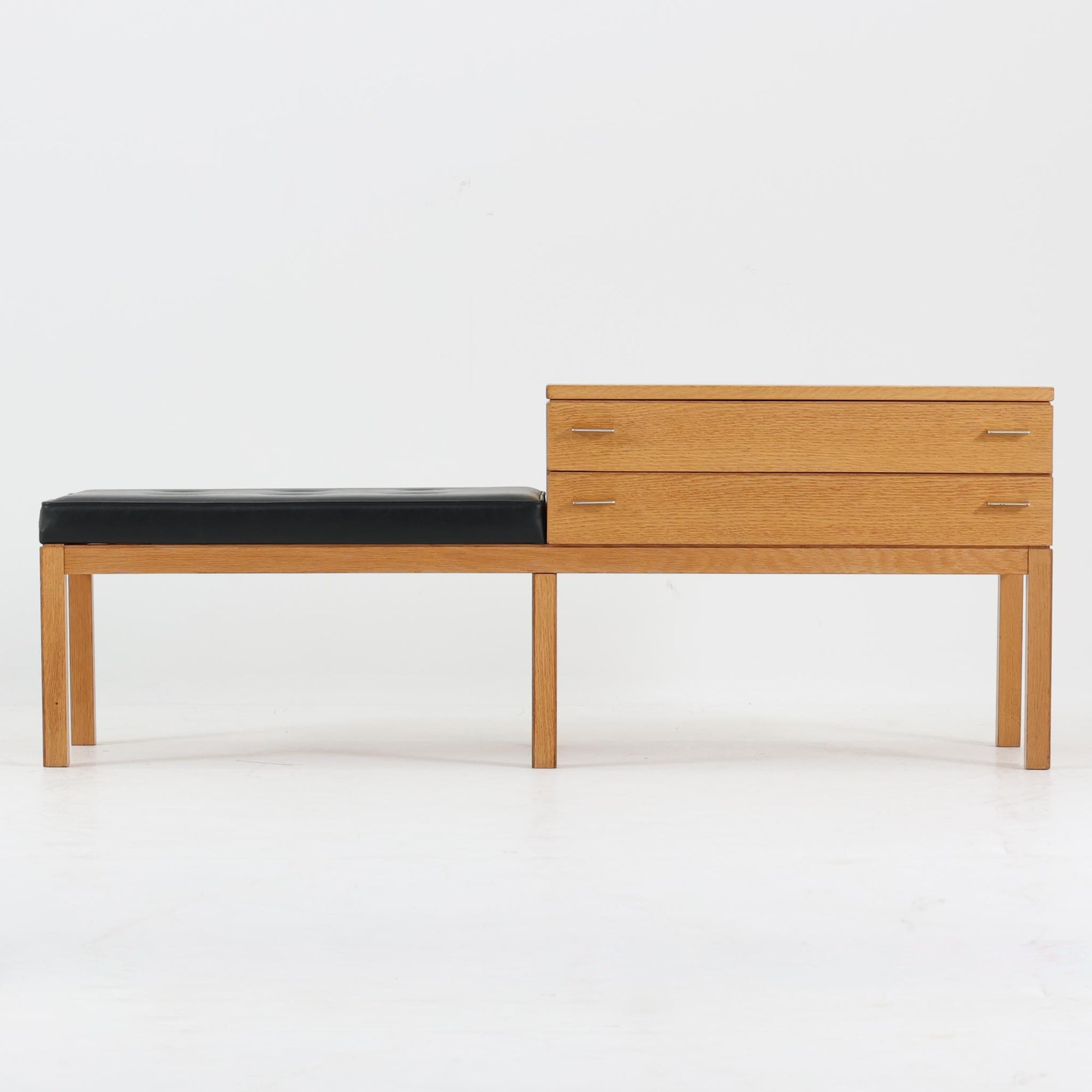 Frosekeが手掛けたTemaシリーズのテレフォンベンチです。オーク材のナチュラルな木目と、ブラックの座面とのコントラストが美しく、空間に引き締まった印象をもたらします。引き出し収納を備えたボックス部とベンチが一体となった構造で、電話台や玄関先での腰掛けとしてはもちろん、小物収納を兼ねた実用的な一台。細身の脚部や控えめなメタルハンドルなど、北欧らしい機能美と軽やかさが魅力です。経年により深みを増した素材感とともに、現代の空間にも自然に溶け込むビンテージならではの存在感をお楽しみいただけます。