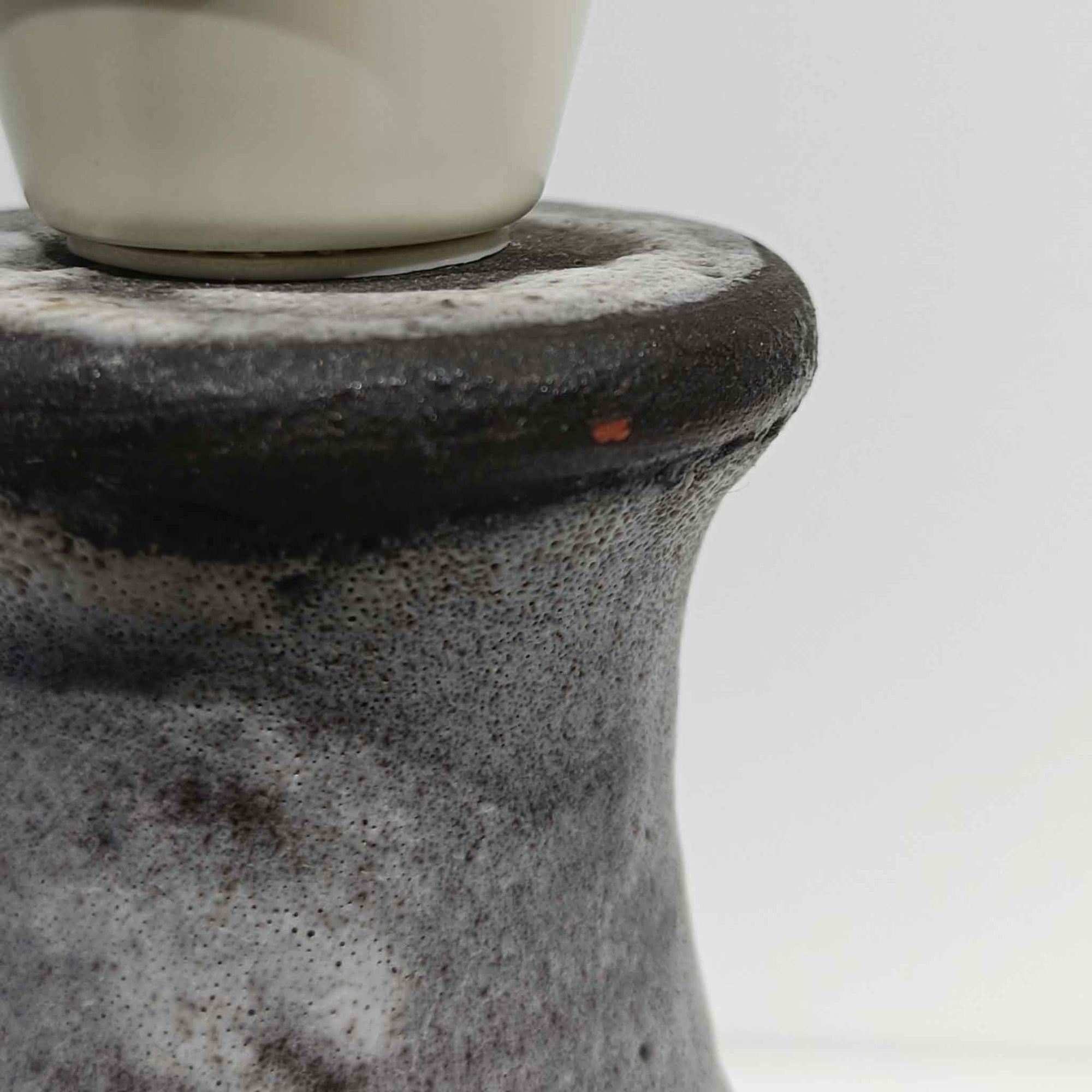 デンマーク製ビンテージテーブルランプです。陶磁器ベースは裾に向かって広がる彫刻的なフォルムを持ち、幾何学的なラインと円形の立体モチーフが規則的に配された、オブジェのような存在感が魅力。マットなグレーを基調とした釉薬に黒の陰影が加わり、手仕事ならではの焼成ムラや表情豊かな質感が際立ちます。リネンシェードから広がるやわらかな灯りが立体意匠を美しく浮かび上がらせ、サイドボードやチェスト、ラウンジ空間のアクセント照明としてもおすすめ。唯一無二の造形美を楽しめる希少なビンテージ品です。