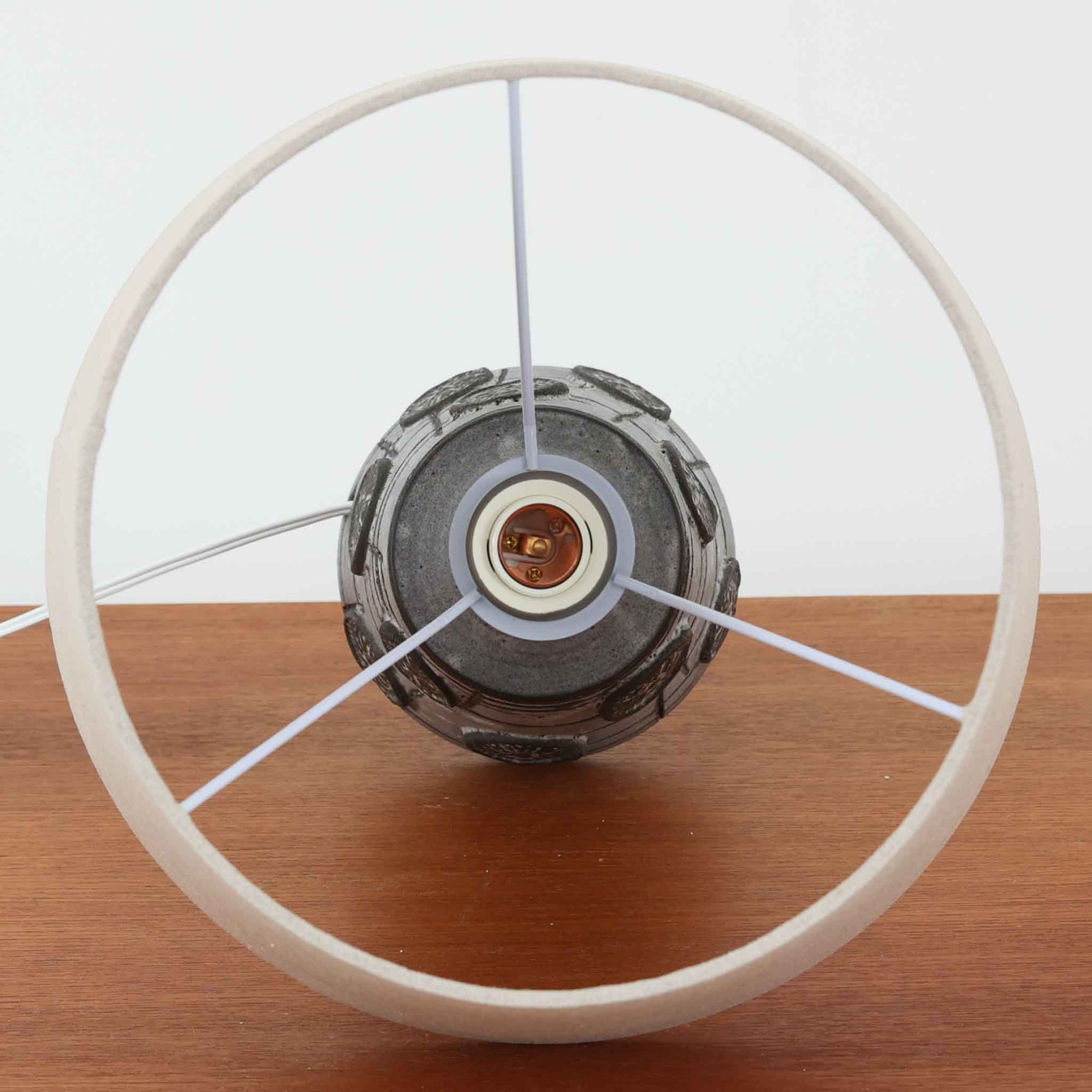 デンマーク製ビンテージテーブルランプです。陶磁器ベースは裾に向かって広がる彫刻的なフォルムを持ち、幾何学的なラインと円形の立体モチーフが規則的に配された、オブジェのような存在感が魅力。マットなグレーを基調とした釉薬に黒の陰影が加わり、手仕事ならではの焼成ムラや表情豊かな質感が際立ちます。リネンシェードから広がるやわらかな灯りが立体意匠を美しく浮かび上がらせ、サイドボードやチェスト、ラウンジ空間のアクセント照明としてもおすすめ。唯一無二の造形美を楽しめる希少なビンテージ品です。