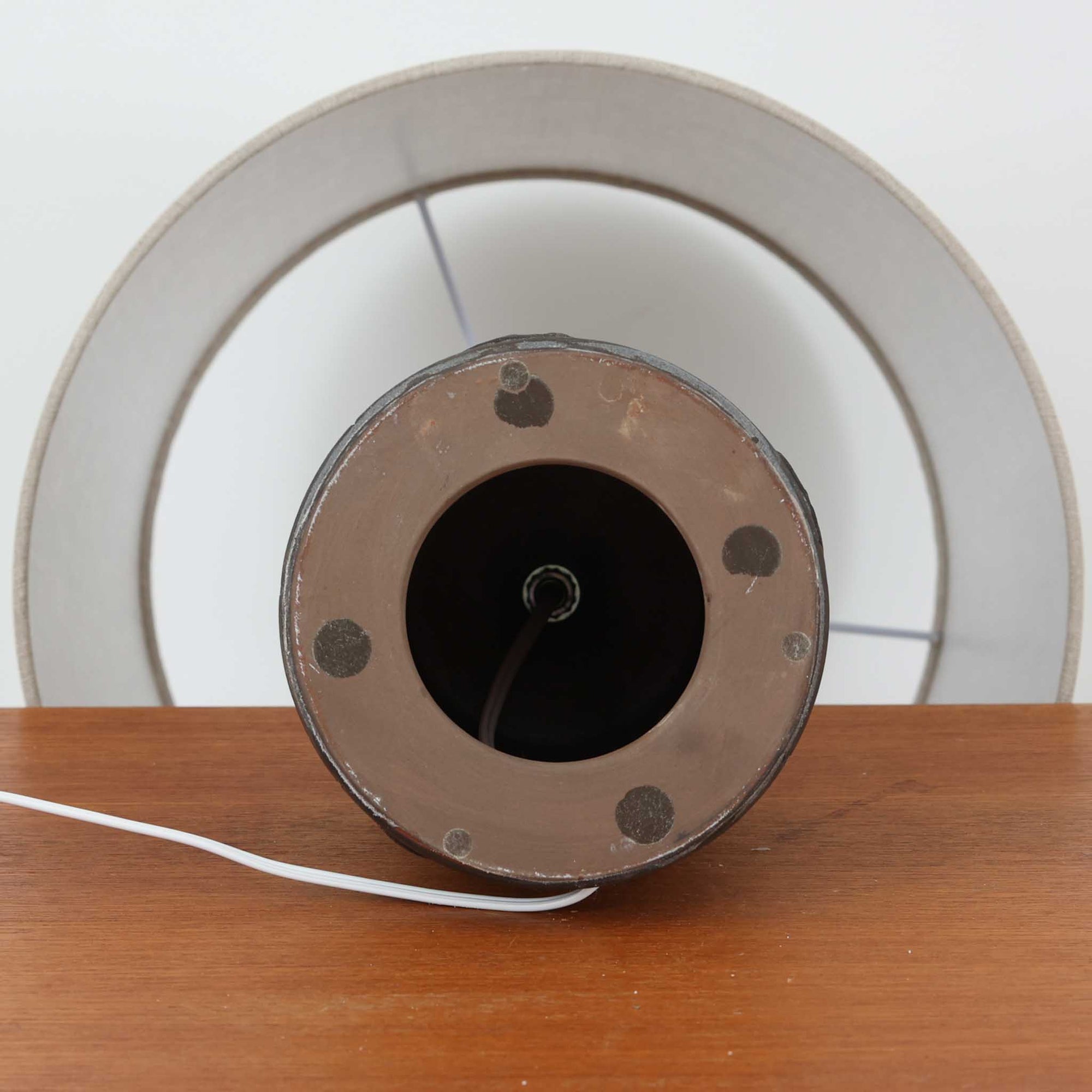 デンマーク製ビンテージテーブルランプです。陶磁器ベースは裾に向かって広がる彫刻的なフォルムを持ち、幾何学的なラインと円形の立体モチーフが規則的に配された、オブジェのような存在感が魅力。マットなグレーを基調とした釉薬に黒の陰影が加わり、手仕事ならではの焼成ムラや表情豊かな質感が際立ちます。リネンシェードから広がるやわらかな灯りが立体意匠を美しく浮かび上がらせ、サイドボードやチェスト、ラウンジ空間のアクセント照明としてもおすすめ。唯一無二の造形美を楽しめる希少なビンテージ品です。