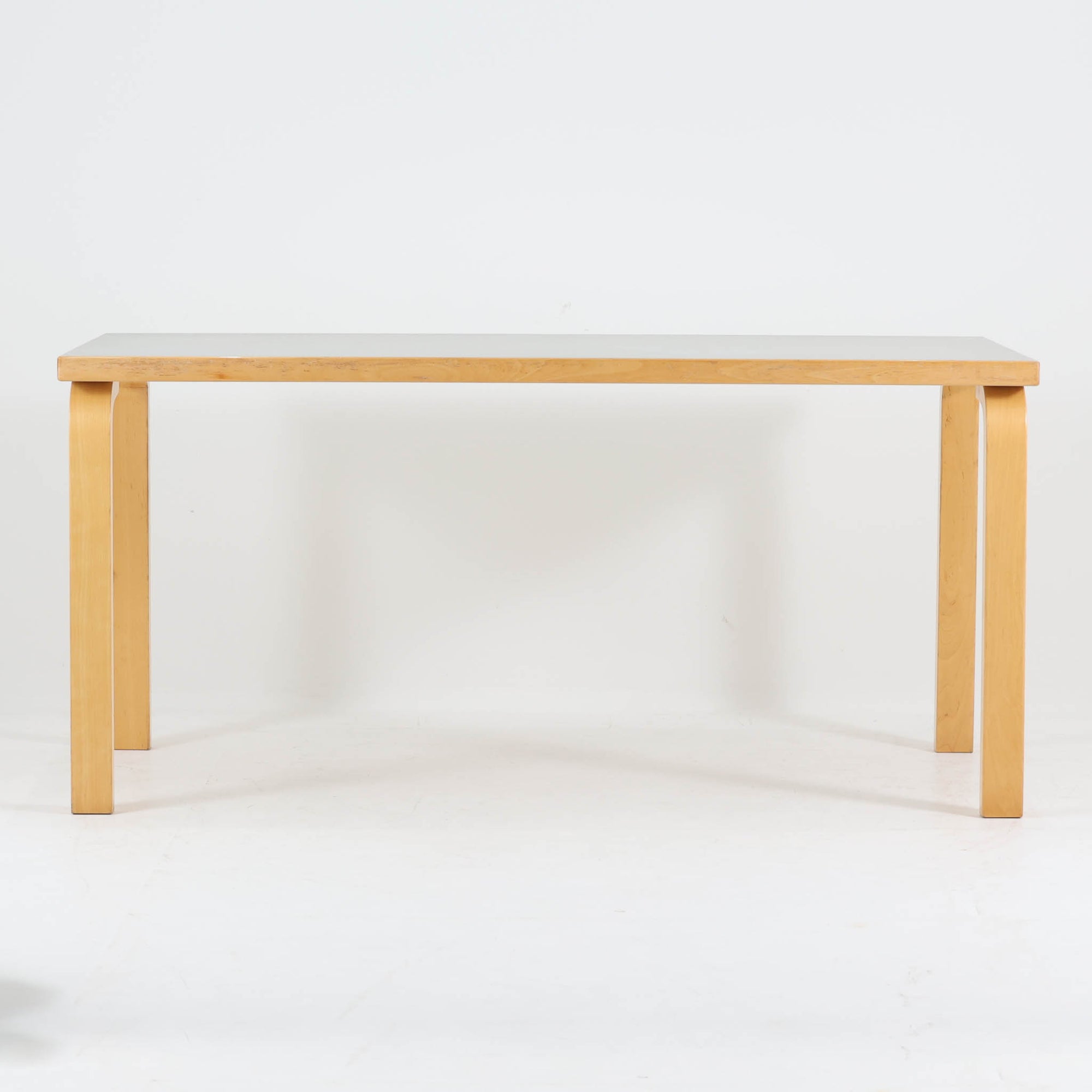 Alvar Aaltoがデザインし、Artekが製作したモデル81Aのダイニングテーブルです。バーチ材の柔らかな木肌とアアルトを象徴するLレッグの曲木構造に、落ち着いたリノリウム天板を組み合わせた、機能美あふれる北欧デザインの名作。幅150cmのゆとりあるサイズは4～6人でのダイニング使用に適しており、ワークスペースやミーティングテーブルとしても活躍します。経年により深みを増した木部の艶やかな風合いと、使い込まれた天板の味わいがビンテージならではの魅力を高め、Artekオリジナルならではの普遍的なデザイン性と希少性が空間に上質な存在感をもたらします。