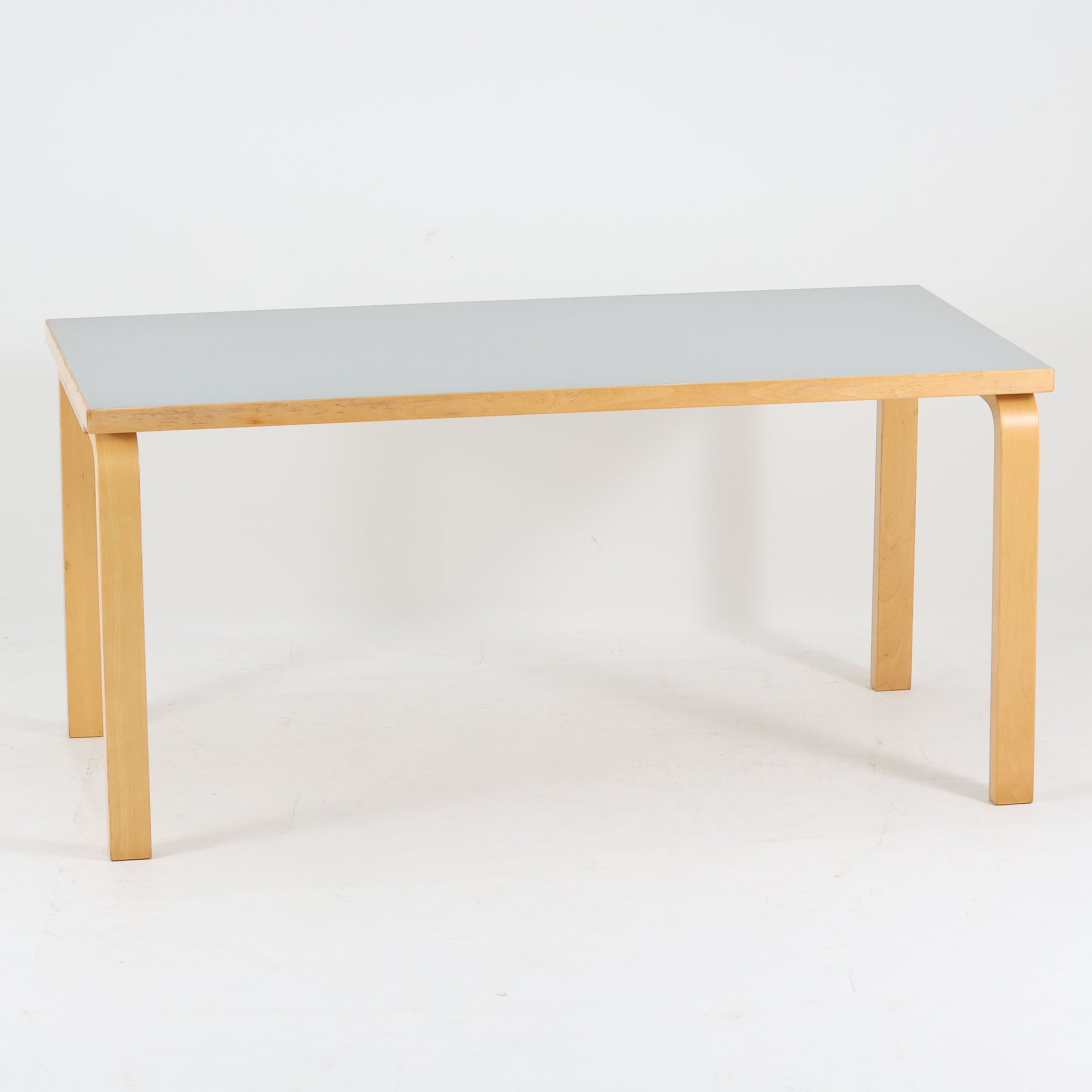 Alvar Aaltoがデザインし、Artekが製作したモデル81Aのダイニングテーブルです。バーチ材の柔らかな木肌とアアルトを象徴するLレッグの曲木構造に、落ち着いたリノリウム天板を組み合わせた、機能美あふれる北欧デザインの名作。幅150cmのゆとりあるサイズは4～6人でのダイニング使用に適しており、ワークスペースやミーティングテーブルとしても活躍します。経年により深みを増した木部の艶やかな風合いと、使い込まれた天板の味わいがビンテージならではの魅力を高め、Artekオリジナルならではの普遍的なデザイン性と希少性が空間に上質な存在感をもたらします。