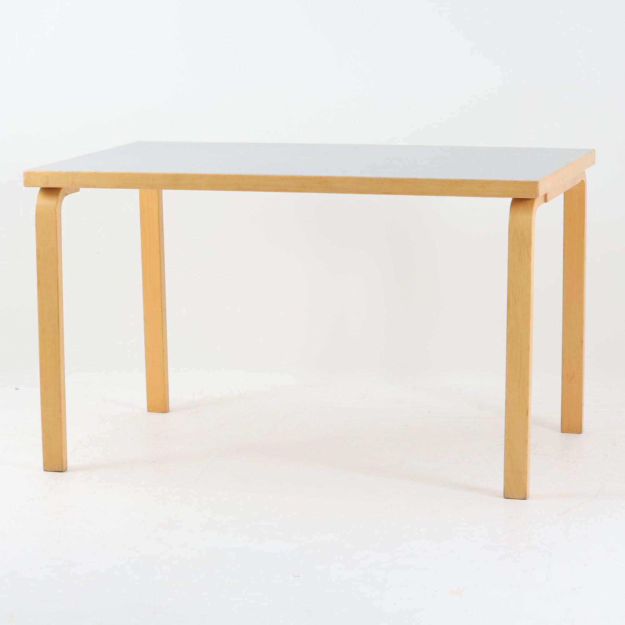 Alvar Aaltoがデザインし、Artek社より製造されたこちらのダイニングテーブルは、落ち着いたグレートーンのリノリウム天板と、美しい木肌を活かしたバーチ材の脚部を組み合わせた、北欧モダンを代表する名作です。L字型に曲げられた脚部は、アアルトらしい柔らかな造形美と高い機能性を兼ね備え、空間に軽やかな印象をもたらします。幅120cmの使い勝手のよいサイズで、ダイニングはもちろんワークスペースにも自然に馴染みます。なお、天板裏面には脚の付け替え跡が確認できたため、安心してお使いいただけるよう現状でしっかり固定しており、脚部の取り外しはできない仕様となっております。