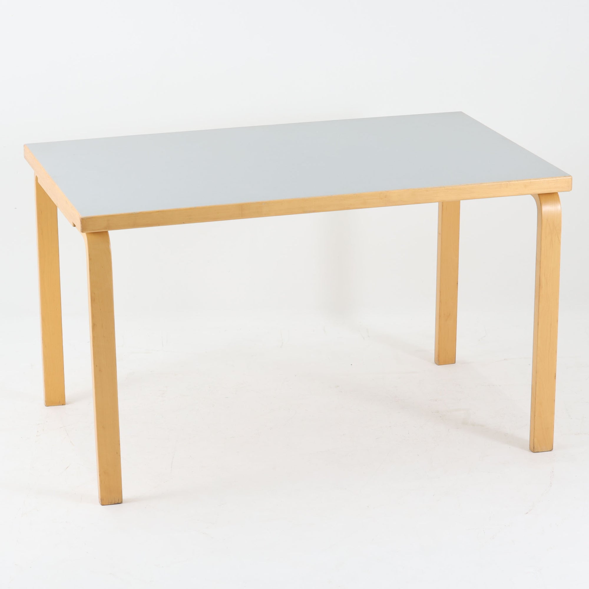 Alvar Aaltoがデザインし、Artek社より製造されたこちらのダイニングテーブルは、落ち着いたグレートーンのリノリウム天板と、美しい木肌を活かしたバーチ材の脚部を組み合わせた、北欧モダンを代表する名作です。L字型に曲げられた脚部は、アアルトらしい柔らかな造形美と高い機能性を兼ね備え、空間に軽やかな印象をもたらします。幅120cmの使い勝手のよいサイズで、ダイニングはもちろんワークスペースにも自然に馴染みます。なお、天板裏面には脚の付け替え跡が確認できたため、安心してお使いいただけるよう現状でしっかり固定しており、脚部の取り外しはできない仕様となっております。