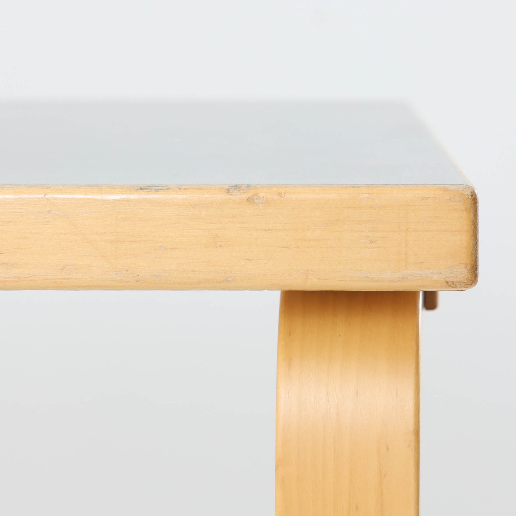 Alvar Aaltoがデザインし、Artek社より製造されたこちらのダイニングテーブルは、落ち着いたグレートーンのリノリウム天板と、美しい木肌を活かしたバーチ材の脚部を組み合わせた、北欧モダンを代表する名作です。L字型に曲げられた脚部は、アアルトらしい柔らかな造形美と高い機能性を兼ね備え、空間に軽やかな印象をもたらします。幅120cmの使い勝手のよいサイズで、ダイニングはもちろんワークスペースにも自然に馴染みます。なお、天板裏面には脚の付け替え跡が確認できたため、安心してお使いいただけるよう現状でしっかり固定しており、脚部の取り外しはできない仕様となっております。
