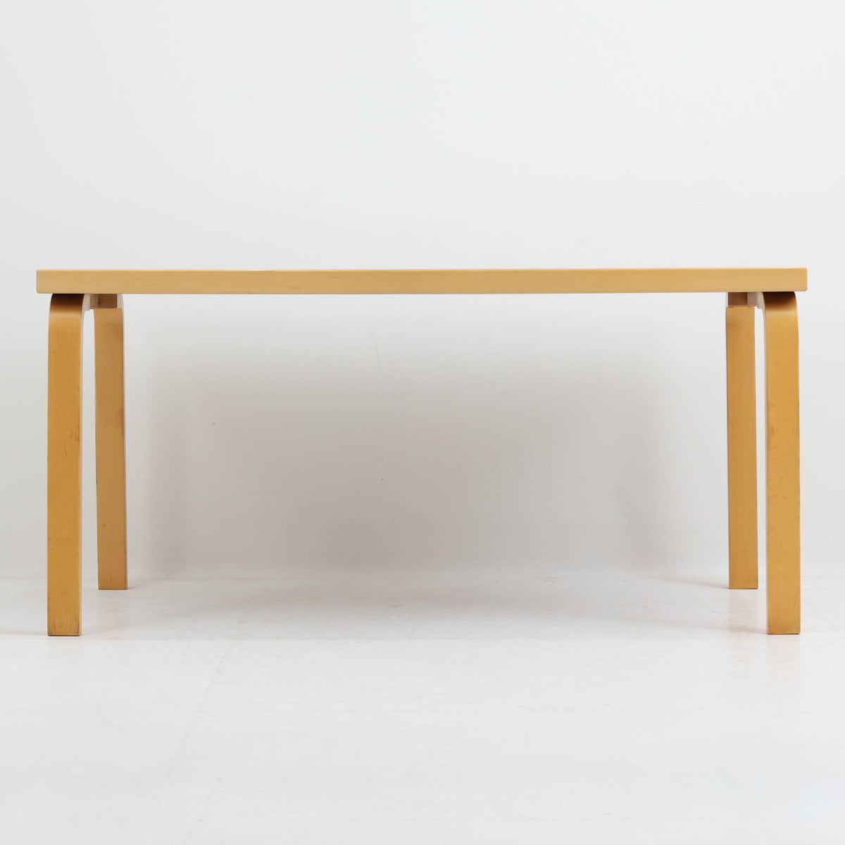 Artek（アルテック）社の「Table 81A」、Alvar Aalto（アルヴァ・アアルト）によるデザインのビンテージダイニングテーブルです。バーチ材を曲げて成形した象徴的なLレッグに、ホワイトのリノリウム天板を組み合わせた端正な佇まいが特徴。装飾を抑えたシンプルな構成ながら、柔らかな脚部の曲線にアアルトらしい造形美が表れています。幅150cmで食卓からワークテーブルまで使いやすく、時代を超えて空間に馴染む普遍的な魅力を備えています。