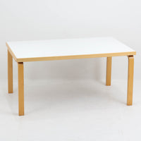 Artek（アルテック）社の「Table 81A」、Alvar Aalto（アルヴァ・アアルト）によるデザインのビンテージダイニングテーブルです。バーチ材を曲げて成形した象徴的なLレッグに、ホワイトのリノリウム天板を組み合わせた端正な佇まいが特徴。装飾を抑えたシンプルな構成ながら、柔らかな脚部の曲線にアアルトらしい造形美が表れています。幅150cmで食卓からワークテーブルまで使いやすく、時代を超えて空間に馴染む普遍的な魅力を備えています。