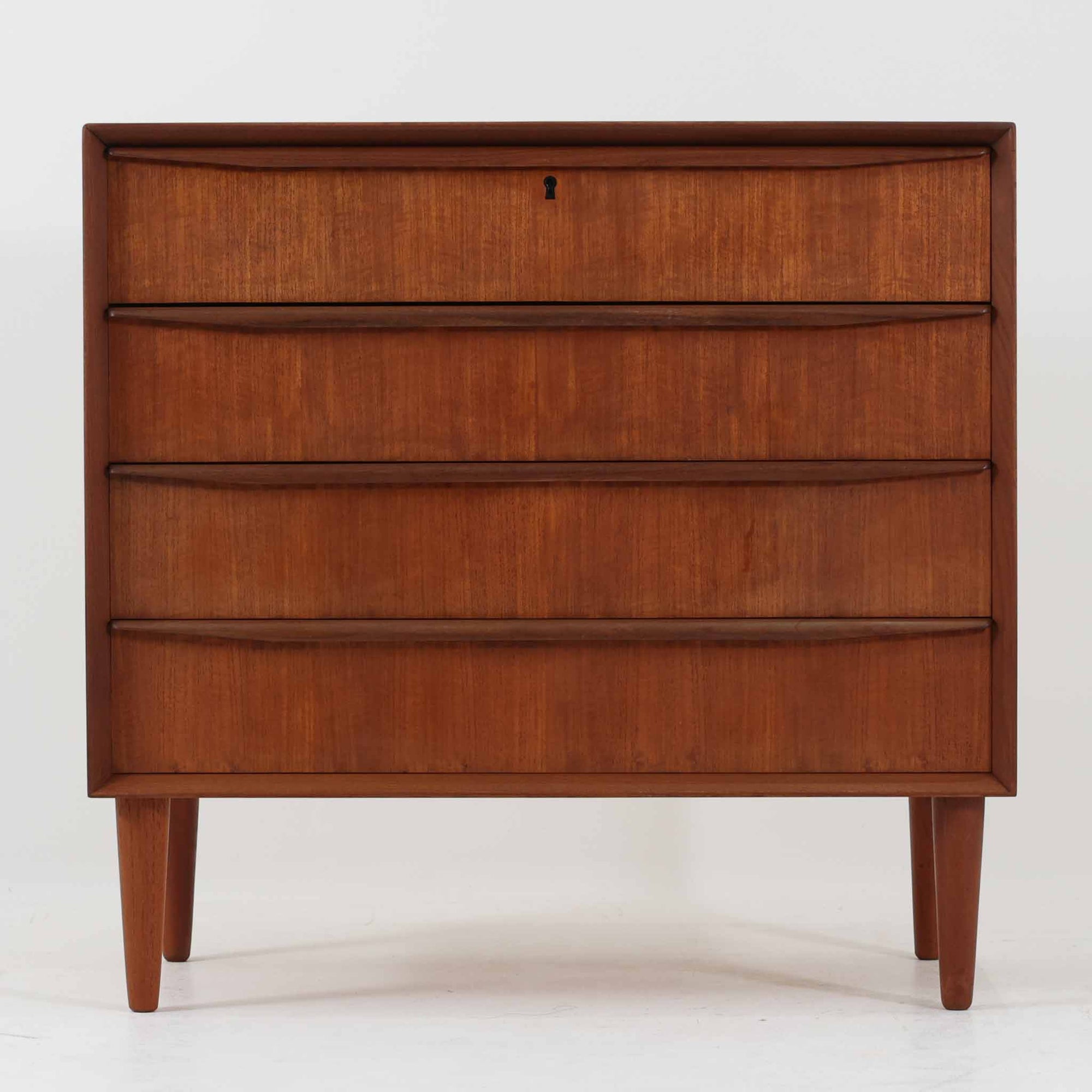 デンマーク製の4段チェストです。チーク材ならではの美しい木目と経年で深みを増した飴色の艶が、空間に落ち着きと上質感をもたらします。引き出し前板には緩やかな削り込みの手掛けが施され、さらに本体外周の縁まで丁寧に削り出された立体的なフレームが上質な陰影を生み出し、北欧家具らしい高い木工クオリティを感じさせます。幅80cmの使いやすいサイズで、衣類収納はもちろん、リビングや寝室での小物整理にも最適。細身のテーパー脚が軽やかな印象を添え、欠け修理跡を含めた一点物ならではの味わいと、ビンテージの希少性を長く楽しめる一台です。