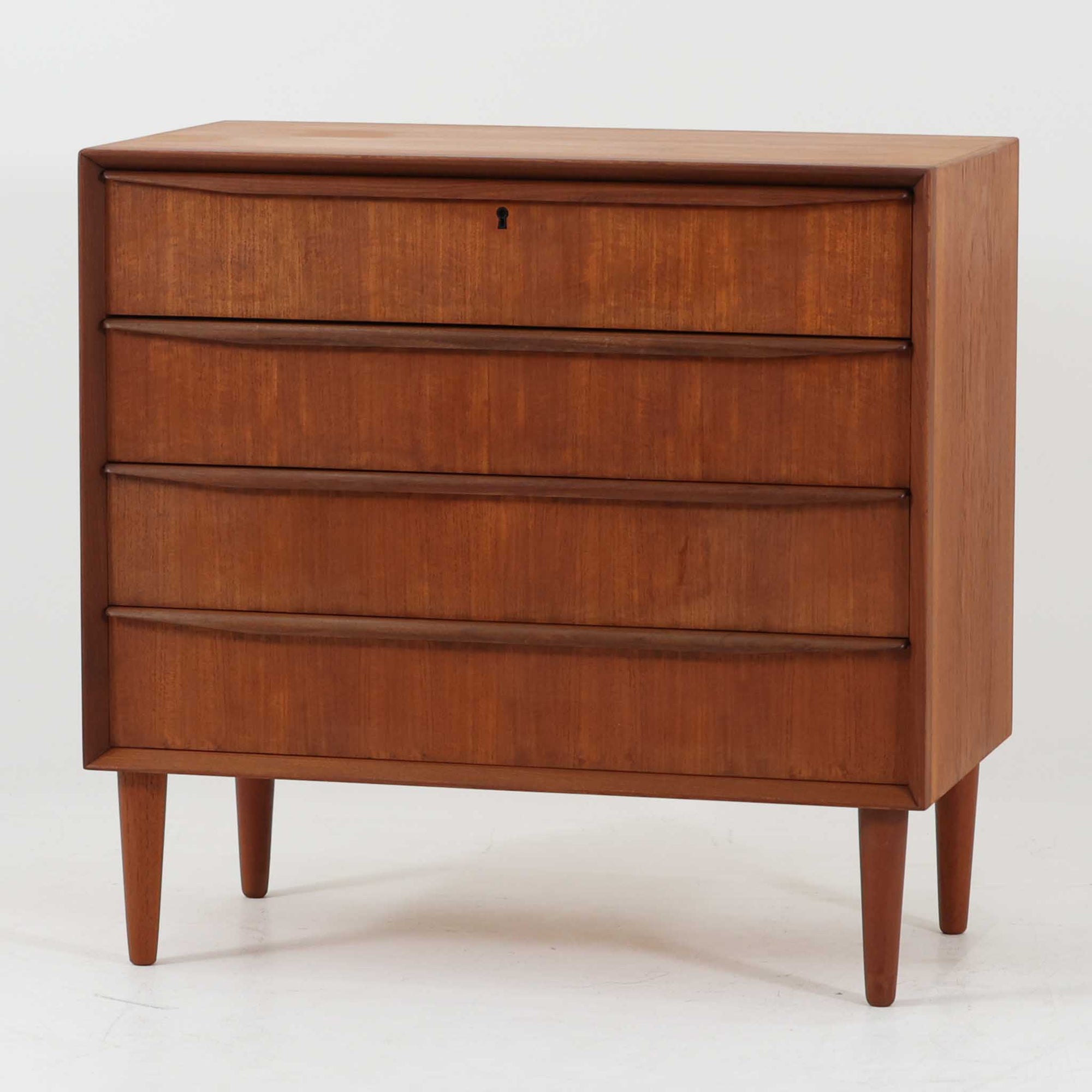 デンマーク製の4段チェストです。チーク材ならではの美しい木目と経年で深みを増した飴色の艶が、空間に落ち着きと上質感をもたらします。引き出し前板には緩やかな削り込みの手掛けが施され、さらに本体外周の縁まで丁寧に削り出された立体的なフレームが上質な陰影を生み出し、北欧家具らしい高い木工クオリティを感じさせます。幅80cmの使いやすいサイズで、衣類収納はもちろん、リビングや寝室での小物整理にも最適。細身のテーパー脚が軽やかな印象を添え、欠け修理跡を含めた一点物ならではの味わいと、ビンテージの希少性を長く楽しめる一台です。