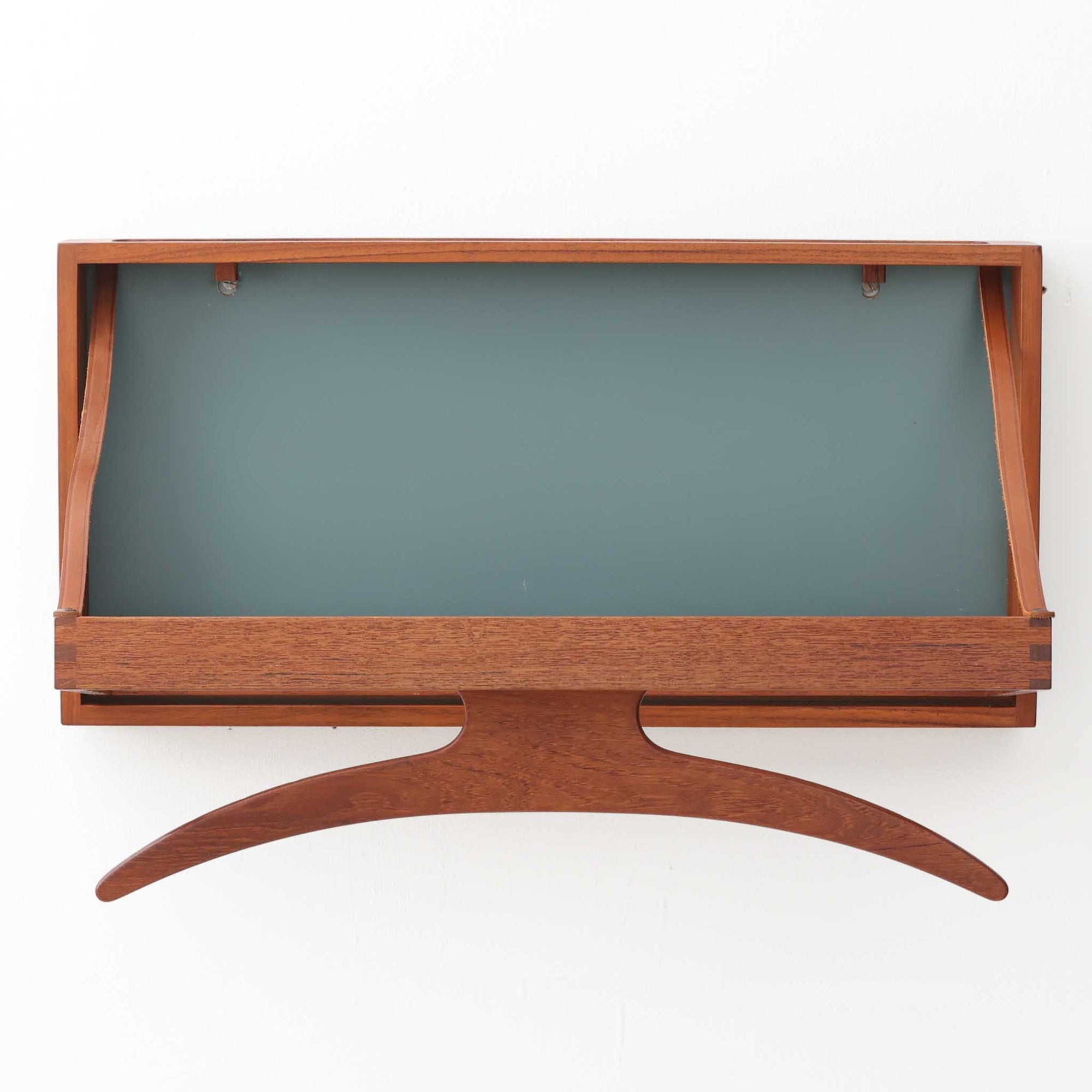 Adam Hoff & Poul Ostergaardがデザインし、Virum Mobelsnickeriにより製作された「The Hanger」ハンガーラックです。チーク材の温かみある木目と、優雅な曲線を描くベースのフォルムが印象的なデザイン。内部にはフックが備えられ、コートや帽子などを掛けて収納できます。フロントのフラップを開くとハンガー部分が現れる機能的な構造で、使用しないときはすっきりとした壁面収納として美しく収まります。革ベルトによる固定や細部の造りにも職人技が感じられる、北欧ビンテージならではの洗練された一品です。