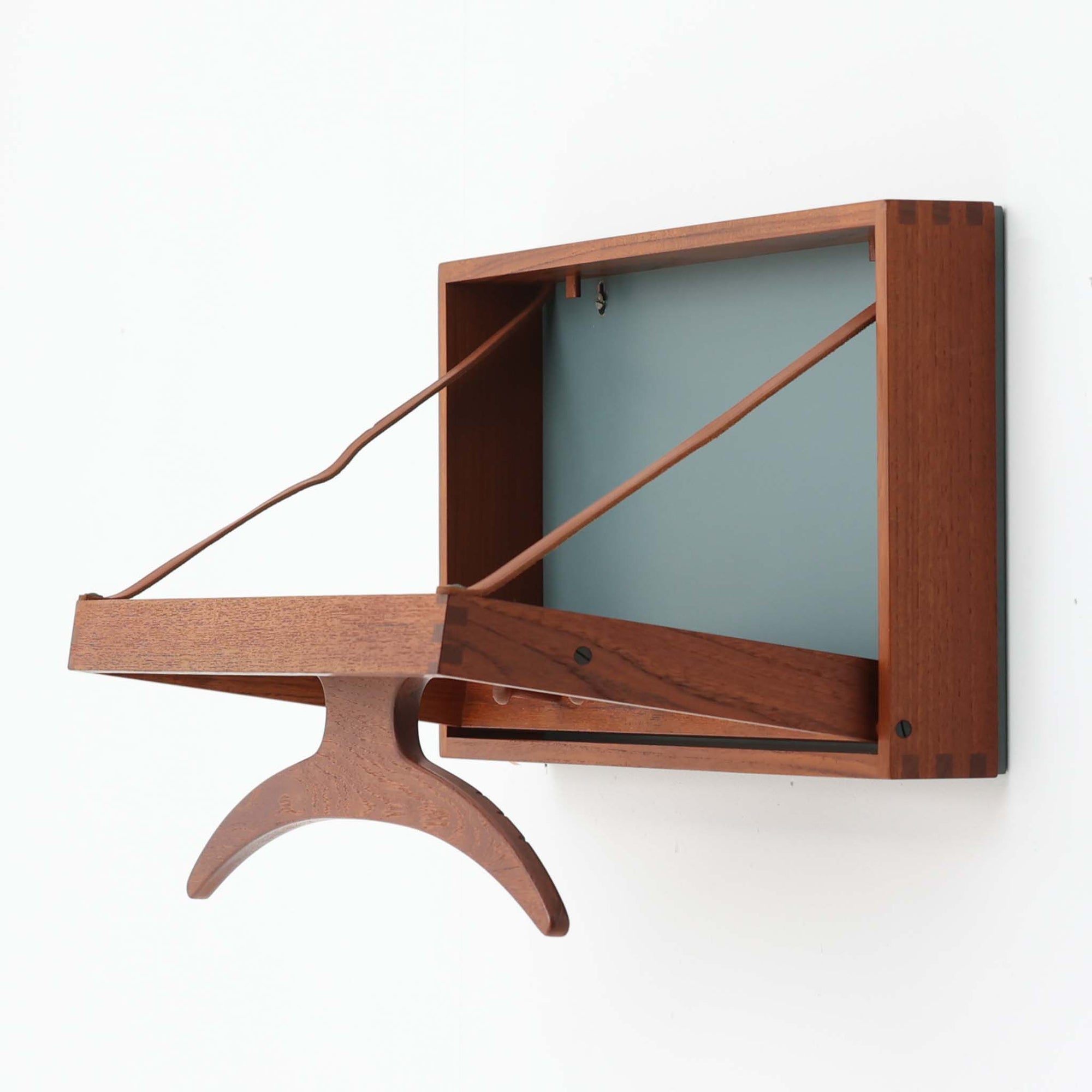 Adam Hoff & Poul Ostergaardがデザインし、Virum Mobelsnickeriにより製作された「The Hanger」ハンガーラックです。チーク材の温かみある木目と、優雅な曲線を描くベースのフォルムが印象的なデザイン。内部にはフックが備えられ、コートや帽子などを掛けて収納できます。フロントのフラップを開くとハンガー部分が現れる機能的な構造で、使用しないときはすっきりとした壁面収納として美しく収まります。革ベルトによる固定や細部の造りにも職人技が感じられる、北欧ビンテージならではの洗練された一品です。