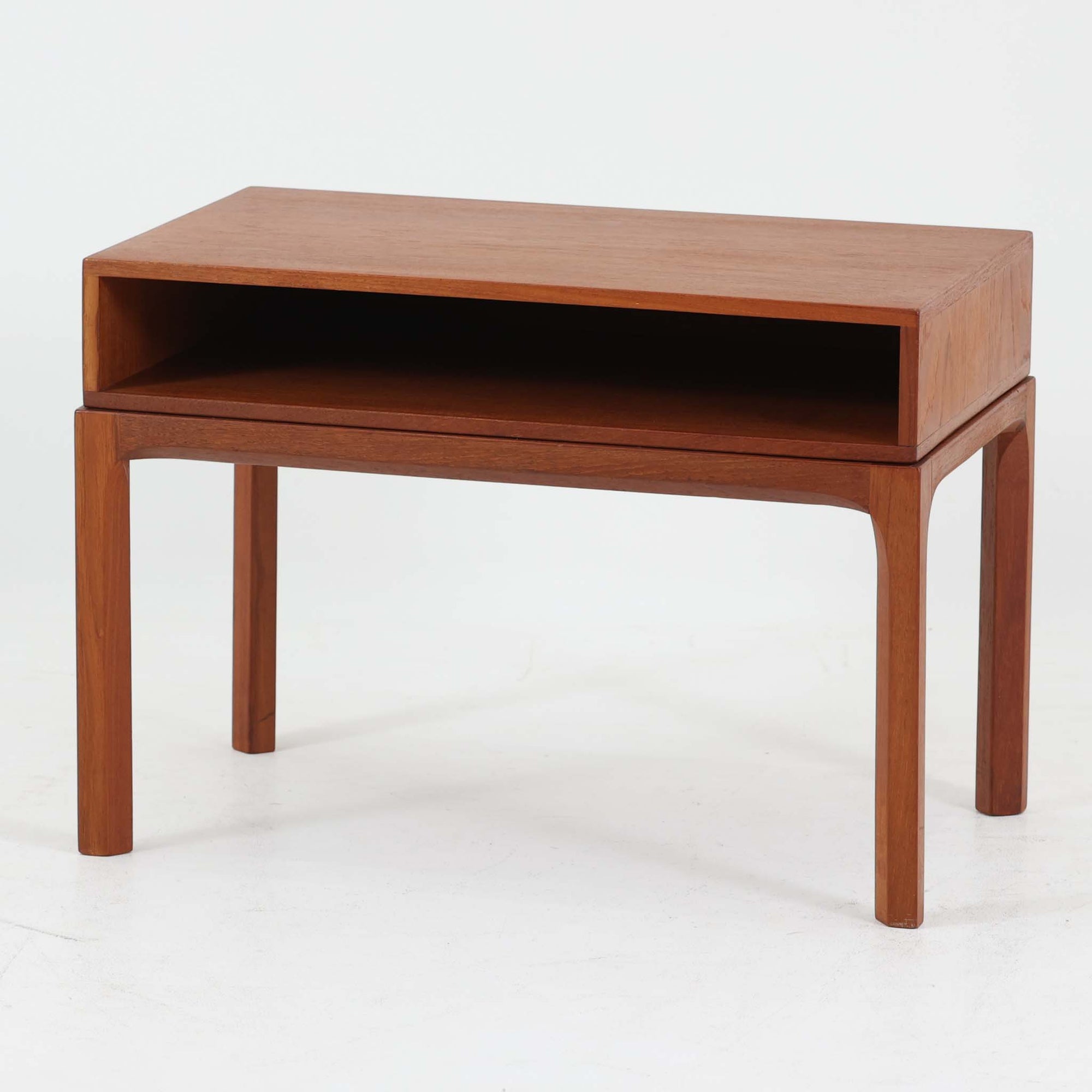 Kai Kristiansenがデザインし、Aksel Kjersgaardが手掛けたNo.383 サイドテーブルです。チーク材の美しい木目と経年により深みを増した色合いが魅力で、天板下に設けられたオープンスペースが軽やかな印象と実用性を兼ね備えています。脚部は内側に滑らかな曲線で接合されており、シンプルながらも洗練された構造美が際立つ一台。ソファサイドやベッドサイドでの使用はもちろん、雑誌や小物をすっきりと収める収納としても活躍します。北欧ビンテージならではの丁寧な木工技術と希少性を感じられる逸品です。