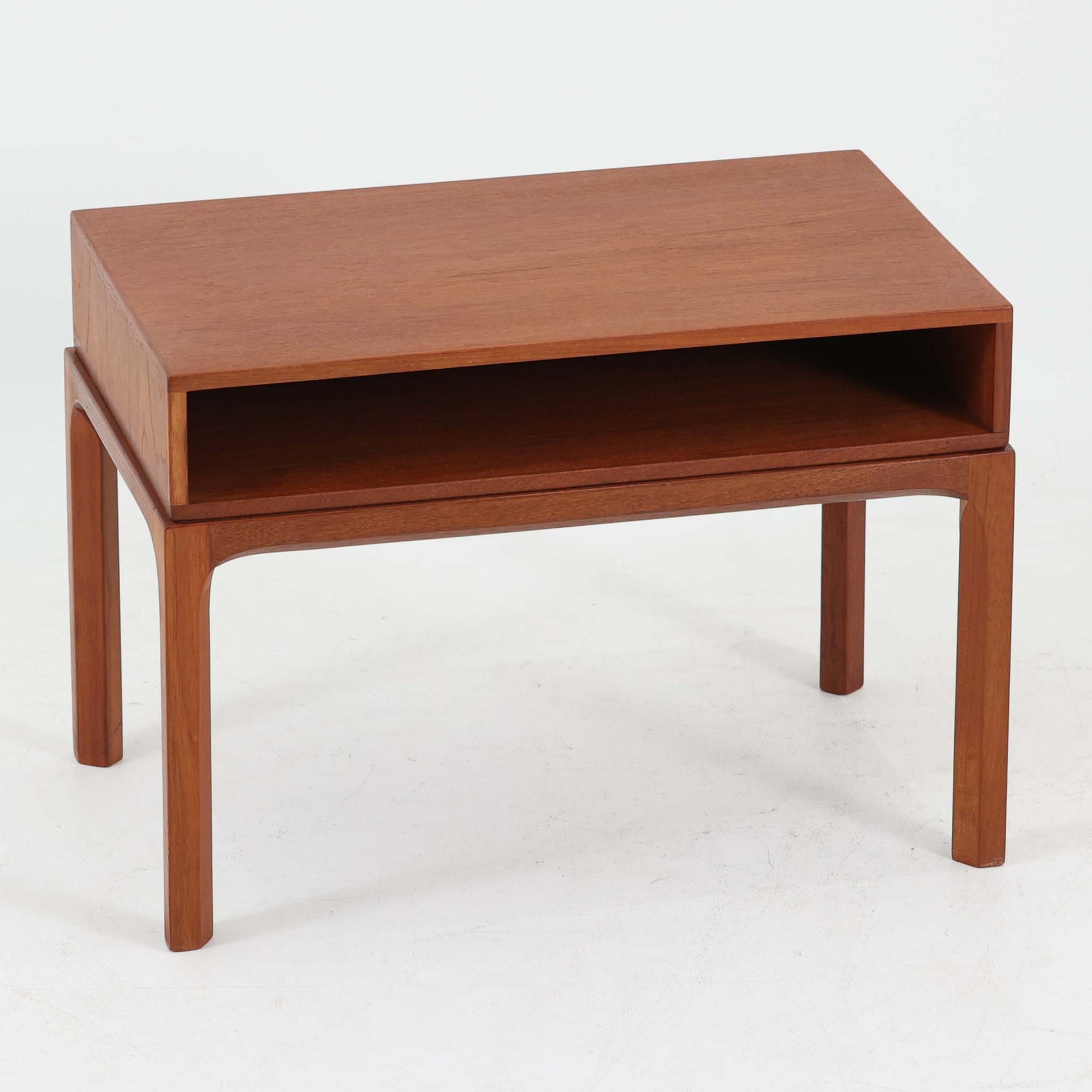 Kai Kristiansenがデザインし、Aksel Kjersgaardが手掛けたNo.383 サイドテーブルです。チーク材の美しい木目と経年により深みを増した色合いが魅力で、天板下に設けられたオープンスペースが軽やかな印象と実用性を兼ね備えています。脚部は内側に滑らかな曲線で接合されており、シンプルながらも洗練された構造美が際立つ一台。ソファサイドやベッドサイドでの使用はもちろん、雑誌や小物をすっきりと収める収納としても活躍します。北欧ビンテージならではの丁寧な木工技術と希少性を感じられる逸品です。