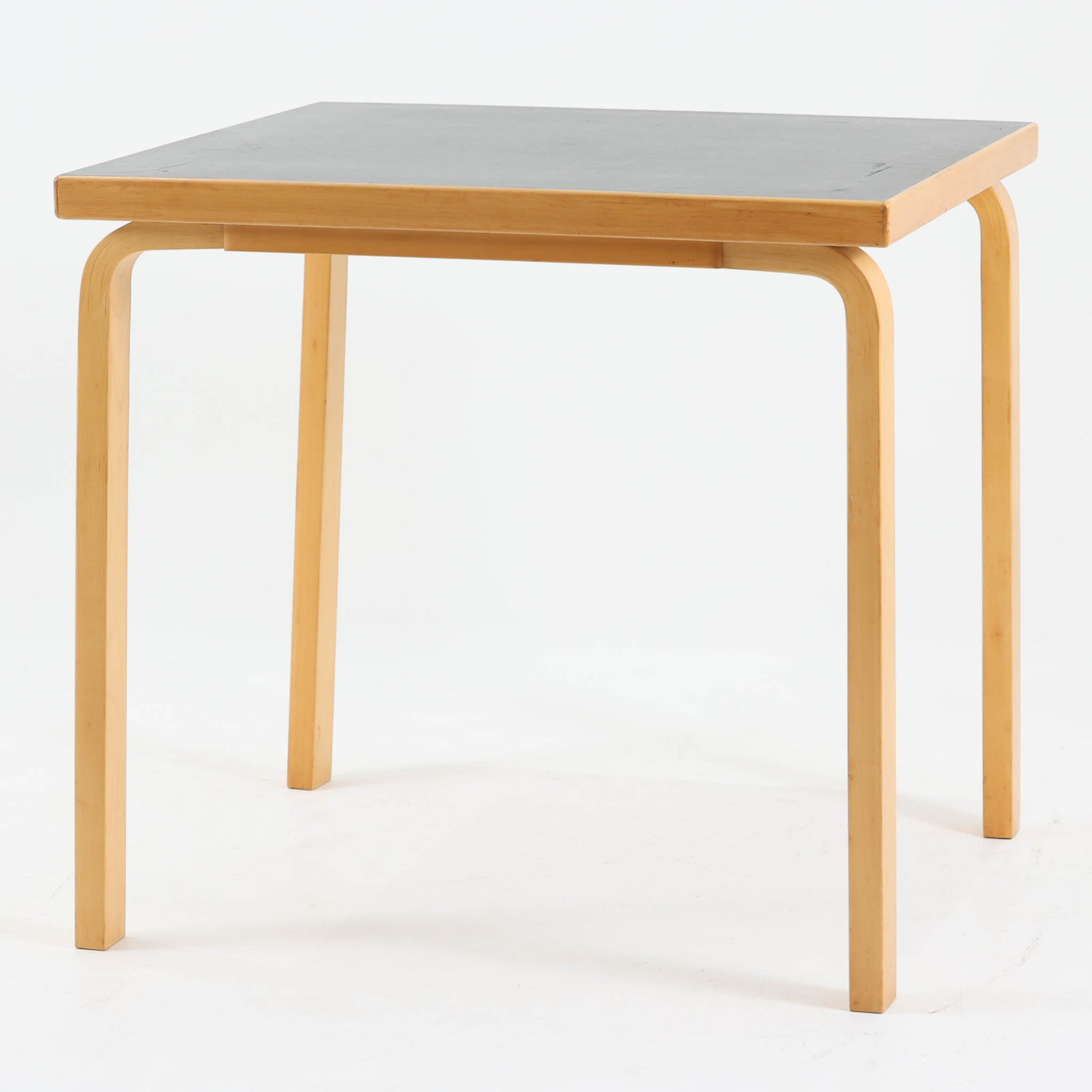 Alvar Aaltoがデザインし、Artekより製作された「81C」ダイニングテーブルです。バーチ材を用いたフレームに、天板には落ち着いた質感のリノリウムを組み合わせたシンプルで機能的なデザインが特徴。脚部にはアアルトを象徴するL字型の曲木構造が採用されており、軽やかで柔らかな印象を与えます。幅75cmの正方形サイズはダイニングはもちろんワークテーブルとしても使いやすく、日常の空間に北欧デザインの美しさと実用性をもたらすビンテージ家具です。本個体は、脚部の5枚レイヤー構造、1973年以降に採用されたプラスネジ、および天板裏の3段構成スタンプの仕様から、1973年～1990年代始めに掛けて製造されたと思われます。