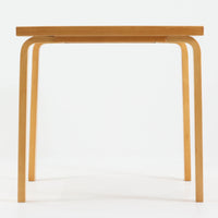 Alvar Aaltoがデザインし、Artekより製作された「81C」ダイニングテーブルです。バーチ材を用いたフレームに、天板には落ち着いた質感のリノリウムを組み合わせたシンプルで機能的なデザインが特徴。脚部にはアアルトを象徴するL字型の曲木構造が採用されており、軽やかで柔らかな印象を与えます。幅75cmの正方形サイズはダイニングはもちろんワークテーブルとしても使いやすく、日常の空間に北欧デザインの美しさと実用性をもたらすビンテージ家具です。本個体は、脚部の5枚レイヤー構造、1973年以降に採用されたプラスネジ、および天板裏の3段構成スタンプの仕様から、1973年～1990年代始めに掛けて製造されたと思われます。