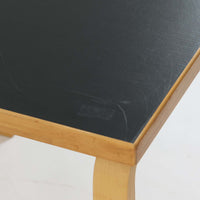 Alvar Aaltoがデザインし、Artekより製作された「81C」ダイニングテーブルです。バーチ材を用いたフレームに、天板には落ち着いた質感のリノリウムを組み合わせたシンプルで機能的なデザインが特徴。脚部にはアアルトを象徴するL字型の曲木構造が採用されており、軽やかで柔らかな印象を与えます。幅75cmの正方形サイズはダイニングはもちろんワークテーブルとしても使いやすく、日常の空間に北欧デザインの美しさと実用性をもたらすビンテージ家具です。本個体は、脚部の5枚レイヤー構造、1973年以降に採用されたプラスネジ、および天板裏の3段構成スタンプの仕様から、1973年～1990年代始めに掛けて製造されたと思われます。