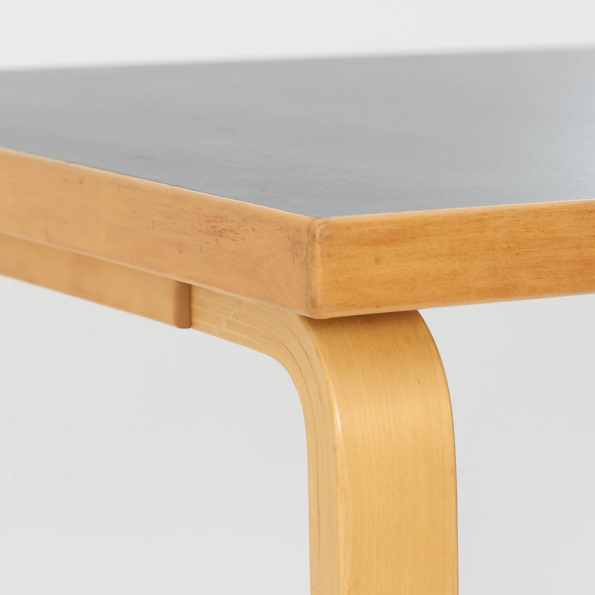 Alvar Aaltoがデザインし、Artekより製作された「81C」ダイニングテーブルです。バーチ材を用いたフレームに、天板には落ち着いた質感のリノリウムを組み合わせたシンプルで機能的なデザインが特徴。脚部にはアアルトを象徴するL字型の曲木構造が採用されており、軽やかで柔らかな印象を与えます。幅75cmの正方形サイズはダイニングはもちろんワークテーブルとしても使いやすく、日常の空間に北欧デザインの美しさと実用性をもたらすビンテージ家具です。本個体は、脚部の5枚レイヤー構造、1973年以降に採用されたプラスネジ、および天板裏の3段構成スタンプの仕様から、1973年～1990年代始めに掛けて製造されたと思われます。