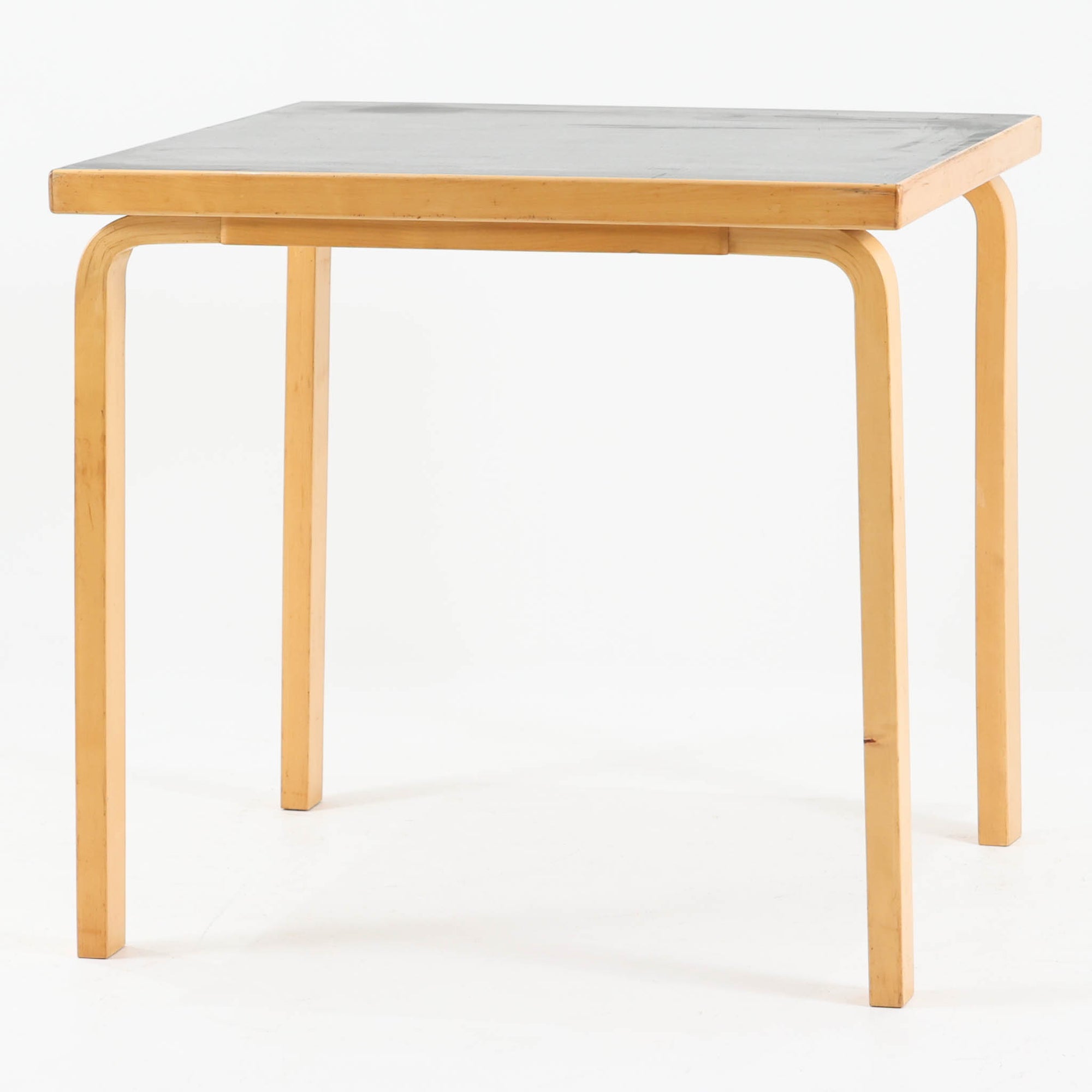 Alvar Aaltoがデザインし、Artekより製作された「81C」ダイニングテーブルです。バーチ材を用いたフレームに、天板には落ち着いた質感のリノリウムを組み合わせたシンプルで機能的なデザインが特徴。脚部にはアアルトを象徴するL字型の曲木構造が採用されており、軽やかで柔らかな印象を与えます。幅75cmの正方形サイズはダイニングはもちろんワークテーブルとしても使いやすく、日常の空間に北欧デザインの美しさと実用性をもたらすビンテージ家具です。本個体は、脚部の5枚レイヤー構造、1973年以降に採用されたプラスネジ、および天板裏の3段構成スタンプの仕様から、1973年～1990年代始めに掛けて製造されたと思われます。