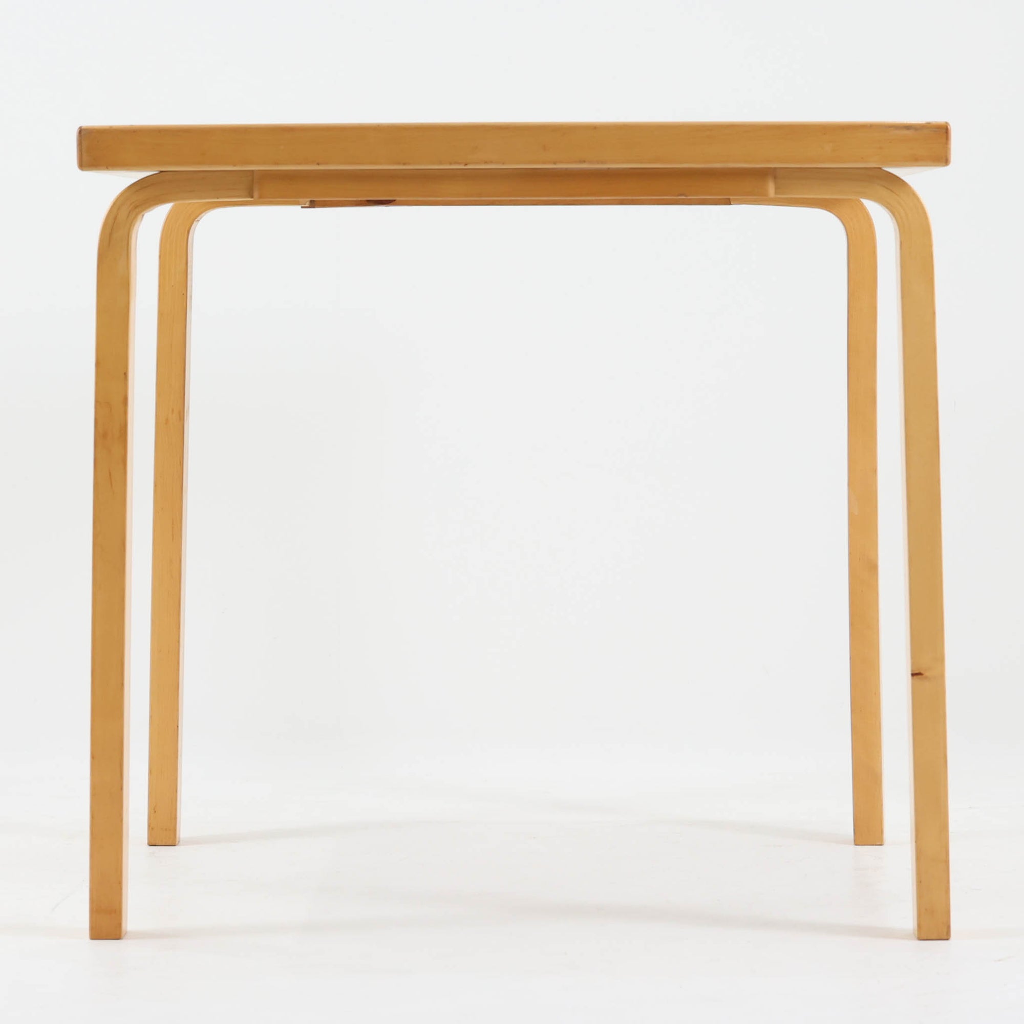 Alvar Aaltoがデザインし、Artekより製作された「81C」ダイニングテーブルです。バーチ材を用いたフレームに、天板には落ち着いた質感のリノリウムを組み合わせたシンプルで機能的なデザインが特徴。脚部にはアアルトを象徴するL字型の曲木構造が採用されており、軽やかで柔らかな印象を与えます。幅75cmの正方形サイズはダイニングはもちろんワークテーブルとしても使いやすく、日常の空間に北欧デザインの美しさと実用性をもたらすビンテージ家具です。本個体は、脚部の5枚レイヤー構造、1973年以降に採用されたプラスネジ、および天板裏の3段構成スタンプの仕様から、1973年～1990年代始めに掛けて製造されたと思われます。