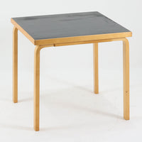 Alvar Aaltoがデザインし、Artekより製作された「81C」ダイニングテーブルです。バーチ材を用いたフレームに、天板には落ち着いた質感のリノリウムを組み合わせたシンプルで機能的なデザインが特徴。脚部にはアアルトを象徴するL字型の曲木構造が採用されており、軽やかで柔らかな印象を与えます。幅75cmの正方形サイズはダイニングはもちろんワークテーブルとしても使いやすく、日常の空間に北欧デザインの美しさと実用性をもたらすビンテージ家具です。本個体は、脚部の5枚レイヤー構造、1973年以降に採用されたプラスネジ、および天板裏の3段構成スタンプの仕様から、1973年～1990年代始めに掛けて製造されたと思われます。