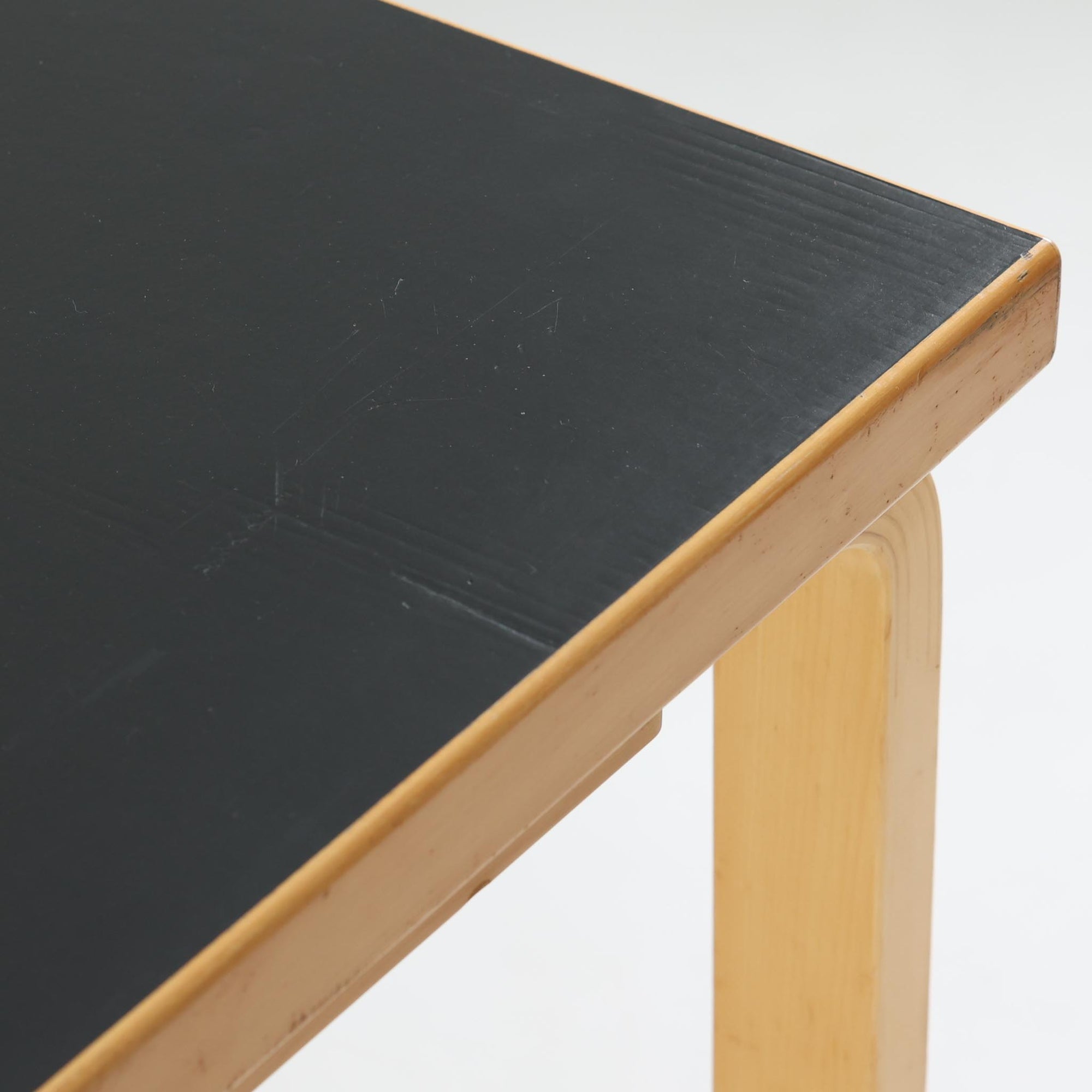 Alvar Aaltoがデザインし、Artekより製作された「81C」ダイニングテーブルです。バーチ材を用いたフレームに、天板には落ち着いた質感のリノリウムを組み合わせたシンプルで機能的なデザインが特徴。脚部にはアアルトを象徴するL字型の曲木構造が採用されており、軽やかで柔らかな印象を与えます。幅75cmの正方形サイズはダイニングはもちろんワークテーブルとしても使いやすく、日常の空間に北欧デザインの美しさと実用性をもたらすビンテージ家具です。本個体は、脚部の5枚レイヤー構造、1973年以降に採用されたプラスネジ、および天板裏の3段構成スタンプの仕様から、1973年～1990年代始めに掛けて製造されたと思われます。