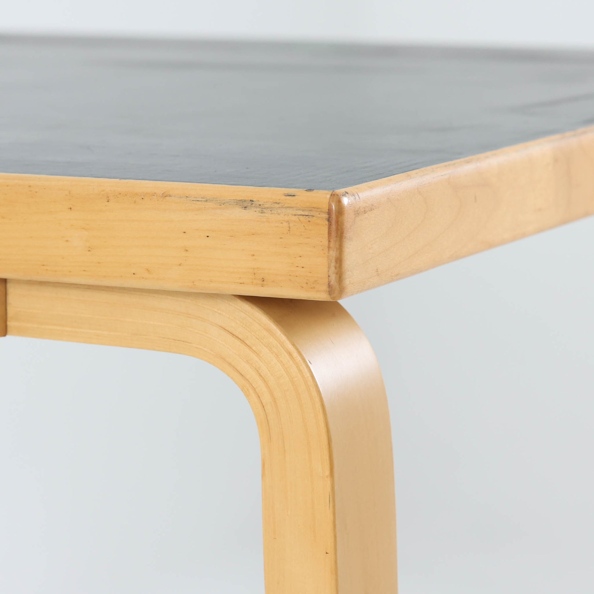 Alvar Aaltoがデザインし、Artekより製作された「81C」ダイニングテーブルです。バーチ材を用いたフレームに、天板には落ち着いた質感のリノリウムを組み合わせたシンプルで機能的なデザインが特徴。脚部にはアアルトを象徴するL字型の曲木構造が採用されており、軽やかで柔らかな印象を与えます。幅75cmの正方形サイズはダイニングはもちろんワークテーブルとしても使いやすく、日常の空間に北欧デザインの美しさと実用性をもたらすビンテージ家具です。本個体は、脚部の5枚レイヤー構造、1973年以降に採用されたプラスネジ、および天板裏の3段構成スタンプの仕様から、1973年～1990年代始めに掛けて製造されたと思われます。