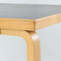 Alvar Aaltoがデザインし、Artekより製作された「81C」ダイニングテーブルです。バーチ材を用いたフレームに、天板には落ち着いた質感のリノリウムを組み合わせたシンプルで機能的なデザインが特徴。脚部にはアアルトを象徴するL字型の曲木構造が採用されており、軽やかで柔らかな印象を与えます。幅75cmの正方形サイズはダイニングはもちろんワークテーブルとしても使いやすく、日常の空間に北欧デザインの美しさと実用性をもたらすビンテージ家具です。本個体は、脚部の5枚レイヤー構造、1973年以降に採用されたプラスネジ、および天板裏の3段構成スタンプの仕様から、1973年～1990年代始めに掛けて製造されたと思われます。