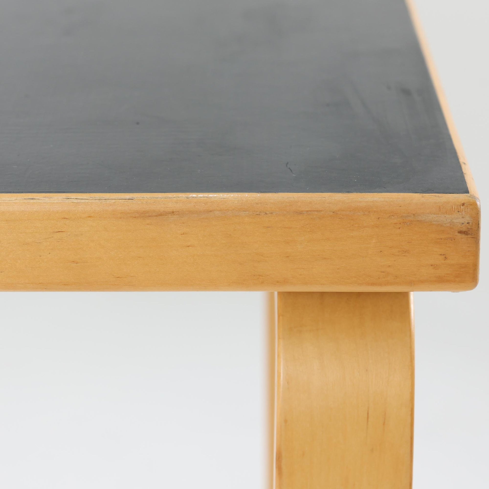 Alvar Aaltoがデザインし、Artekより製作された「81C」ダイニングテーブルです。バーチ材を用いたフレームに、天板には落ち着いた質感のリノリウムを組み合わせたシンプルで機能的なデザインが特徴。脚部にはアアルトを象徴するL字型の曲木構造が採用されており、軽やかで柔らかな印象を与えます。幅75cmの正方形サイズはダイニングはもちろんワークテーブルとしても使いやすく、日常の空間に北欧デザインの美しさと実用性をもたらすビンテージ家具です。本個体は、脚部の5枚レイヤー構造、1973年以降に採用されたプラスネジ、および天板裏の3段構成スタンプの仕様から、1973年～1990年代始めに掛けて製造されたと思われます。