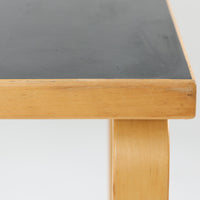 Alvar Aaltoがデザインし、Artekより製作された「81C」ダイニングテーブルです。バーチ材を用いたフレームに、天板には落ち着いた質感のリノリウムを組み合わせたシンプルで機能的なデザインが特徴。脚部にはアアルトを象徴するL字型の曲木構造が採用されており、軽やかで柔らかな印象を与えます。幅75cmの正方形サイズはダイニングはもちろんワークテーブルとしても使いやすく、日常の空間に北欧デザインの美しさと実用性をもたらすビンテージ家具です。本個体は、脚部の5枚レイヤー構造、1973年以降に採用されたプラスネジ、および天板裏の3段構成スタンプの仕様から、1973年～1990年代始めに掛けて製造されたと思われます。