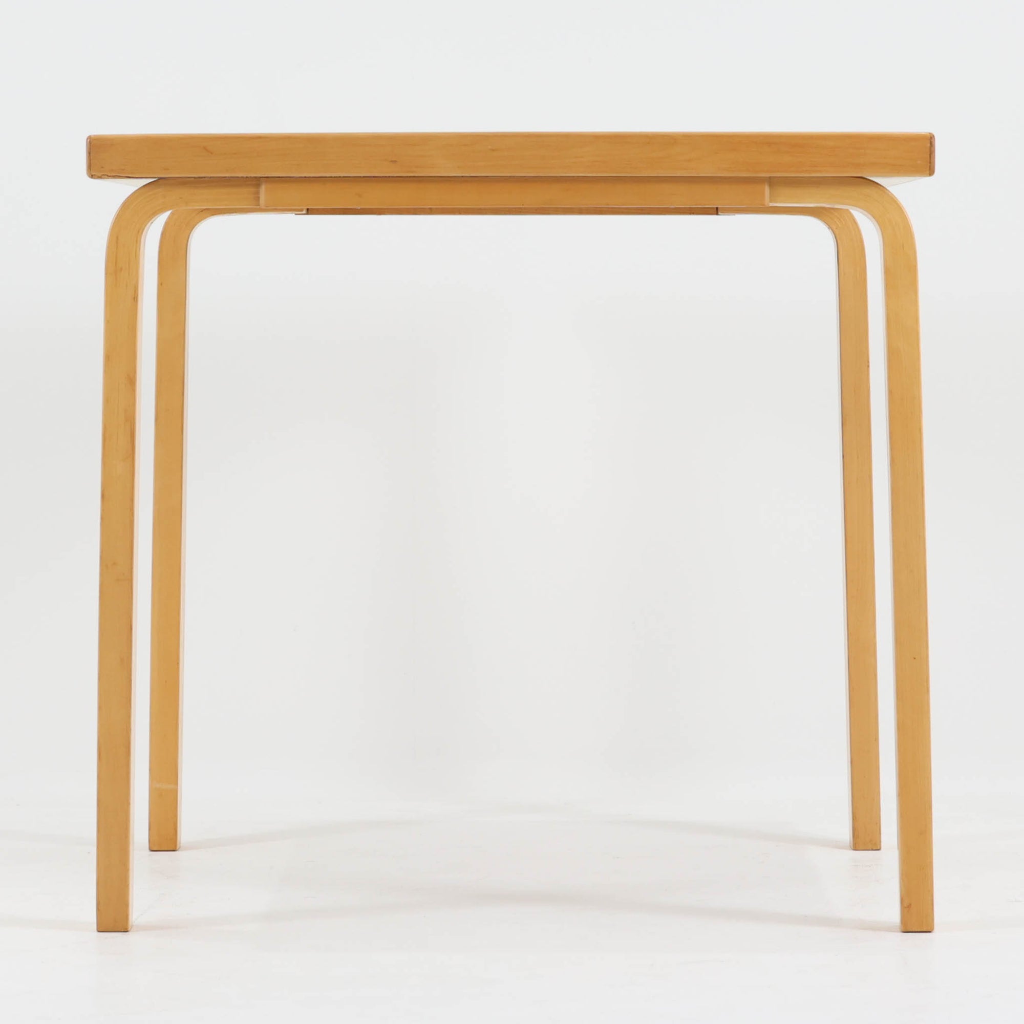 Alvar Aaltoがデザインし、Artekより製作された「81C」ダイニングテーブルです。バーチ材を用いたフレームに、天板には落ち着いた質感のリノリウムを組み合わせたシンプルで機能的なデザインが特徴。脚部にはアアルトを象徴するL字型の曲木構造が採用されており、軽やかで柔らかな印象を与えます。幅75cmの正方形サイズはダイニングはもちろんワークテーブルとしても使いやすく、日常の空間に北欧デザインの美しさと実用性をもたらすビンテージ家具です。本個体は、脚部の5枚レイヤー構造、1973年以降に採用されたプラスネジ、および天板裏の3段構成スタンプの仕様から、1973年～1990年代始めに掛けて製造されたと思われます。