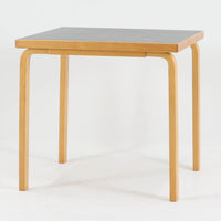 Alvar Aaltoがデザインし、Artekより製作された「81C」ダイニングテーブルです。バーチ材を用いたフレームに、天板には落ち着いた質感のリノリウムを組み合わせたシンプルで機能的なデザインが特徴。脚部にはアアルトを象徴するL字型の曲木構造が採用されており、軽やかで柔らかな印象を与えます。幅75cmの正方形サイズはダイニングはもちろんワークテーブルとしても使いやすく、日常の空間に北欧デザインの美しさと実用性をもたらすビンテージ家具です。本個体は、脚部の5枚レイヤー構造、1973年以降に採用されたプラスネジ、および天板裏の3段構成スタンプの仕様から、1973年～1990年代始めに掛けて製造されたと思われます。