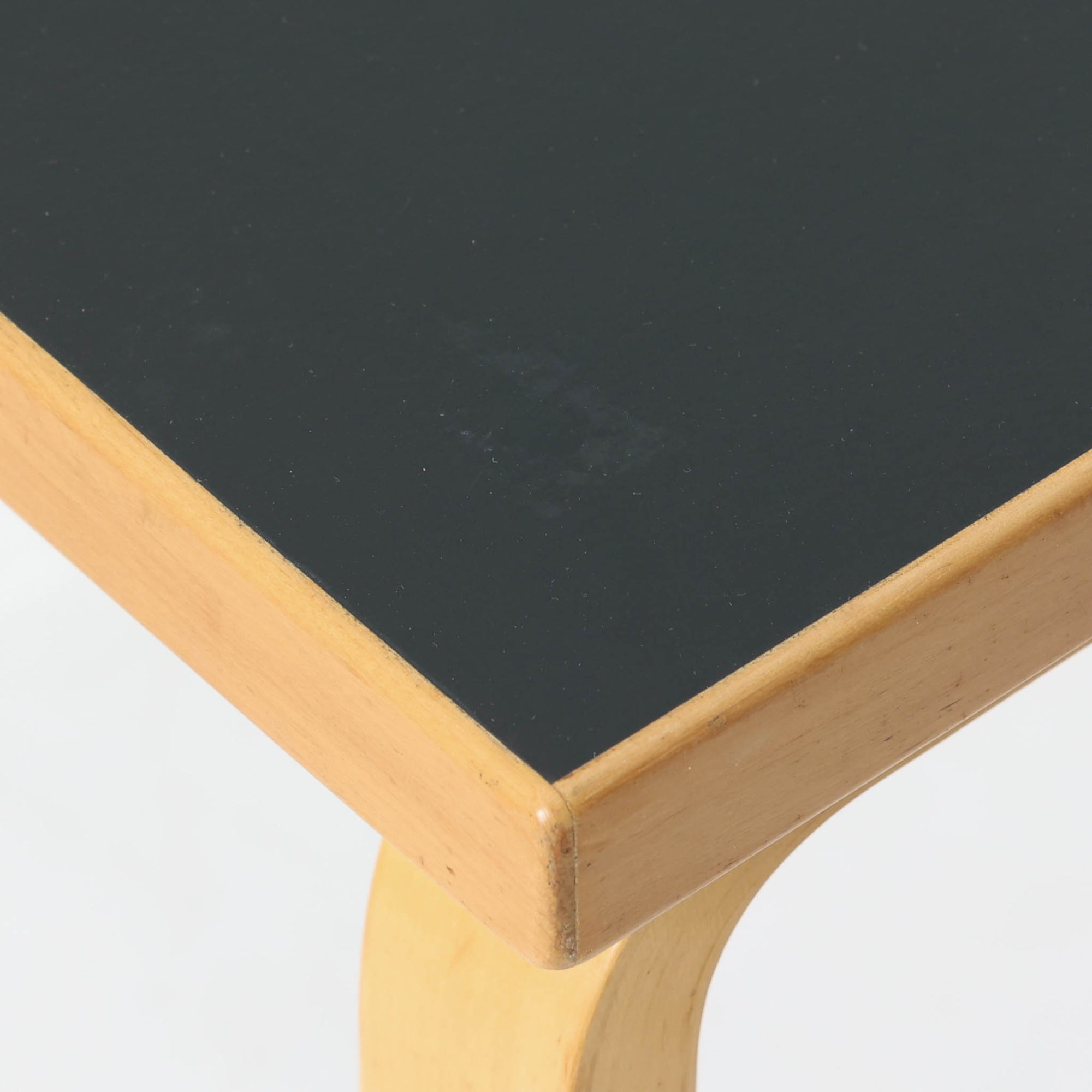 Alvar Aaltoがデザインし、Artekより製作された「81C」ダイニングテーブルです。バーチ材を用いたフレームに、天板には落ち着いた質感のリノリウムを組み合わせたシンプルで機能的なデザインが特徴。脚部にはアアルトを象徴するL字型の曲木構造が採用されており、軽やかで柔らかな印象を与えます。幅75cmの正方形サイズはダイニングはもちろんワークテーブルとしても使いやすく、日常の空間に北欧デザインの美しさと実用性をもたらすビンテージ家具です。本個体は、脚部の5枚レイヤー構造、1973年以降に採用されたプラスネジ、および天板裏の3段構成スタンプの仕様から、1973年～1990年代始めに掛けて製造されたと思われます。