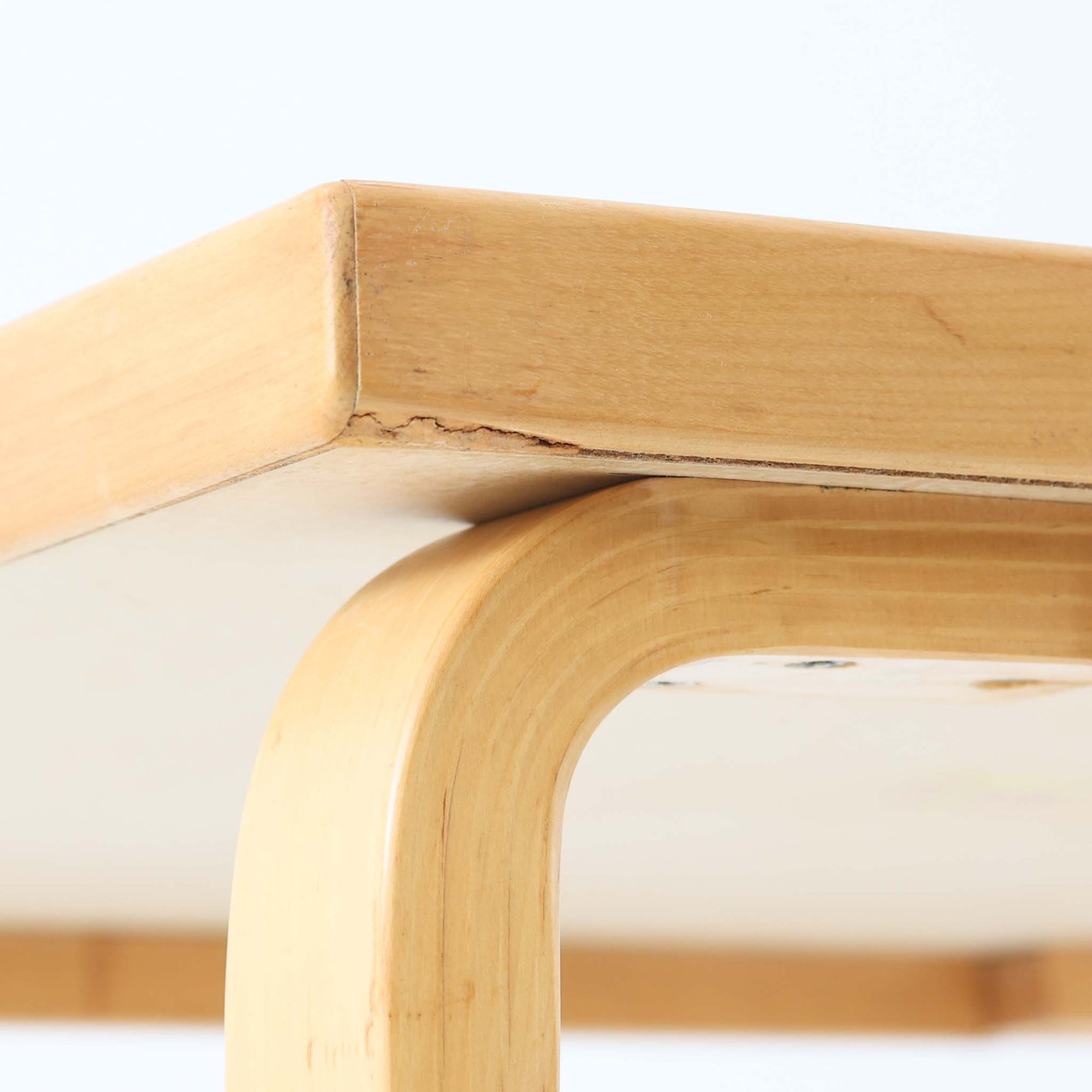 Alvar Aaltoがデザインし、Artekより製作された「81C」ダイニングテーブルです。バーチ材を用いたフレームに、天板には落ち着いた質感のリノリウムを組み合わせたシンプルで機能的なデザインが特徴。脚部にはアアルトを象徴するL字型の曲木構造が採用されており、軽やかで柔らかな印象を与えます。幅75cmの正方形サイズはダイニングはもちろんワークテーブルとしても使いやすく、日常の空間に北欧デザインの美しさと実用性をもたらすビンテージ家具です。本個体は、脚部の5枚レイヤー構造、1973年以降に採用されたプラスネジ、および天板裏の3段構成スタンプの仕様から、1973年～1990年代始めに掛けて製造されたと思われます。