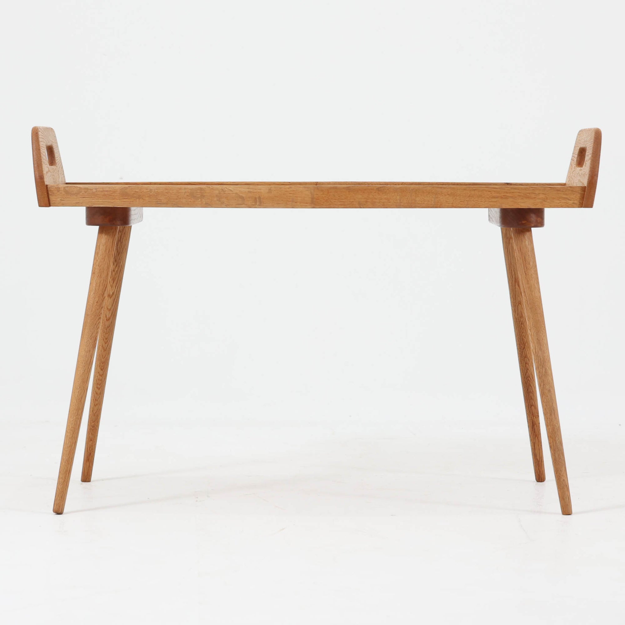 プランターテーブルです。オーク材の温かな木目を活かしたフレームに、淡い色合いのラミネート天板を組み合わせた、北欧らしい軽やかな佇まいが魅力。中央に緩やかな山型を描くユニークな天板形状と、両端の持ち手付きパネル、すらりと伸びるテーパー脚が美しく、置くだけで空間にリズムを生み出します。植物やオブジェを飾るディスプレイ台としてはもちろん、ソファ横のサイドテーブルや玄関先の花台としても使いやすい一台。経年で深みを増した木部の風合いが、ビンテージならではの存在感を引き立てています。