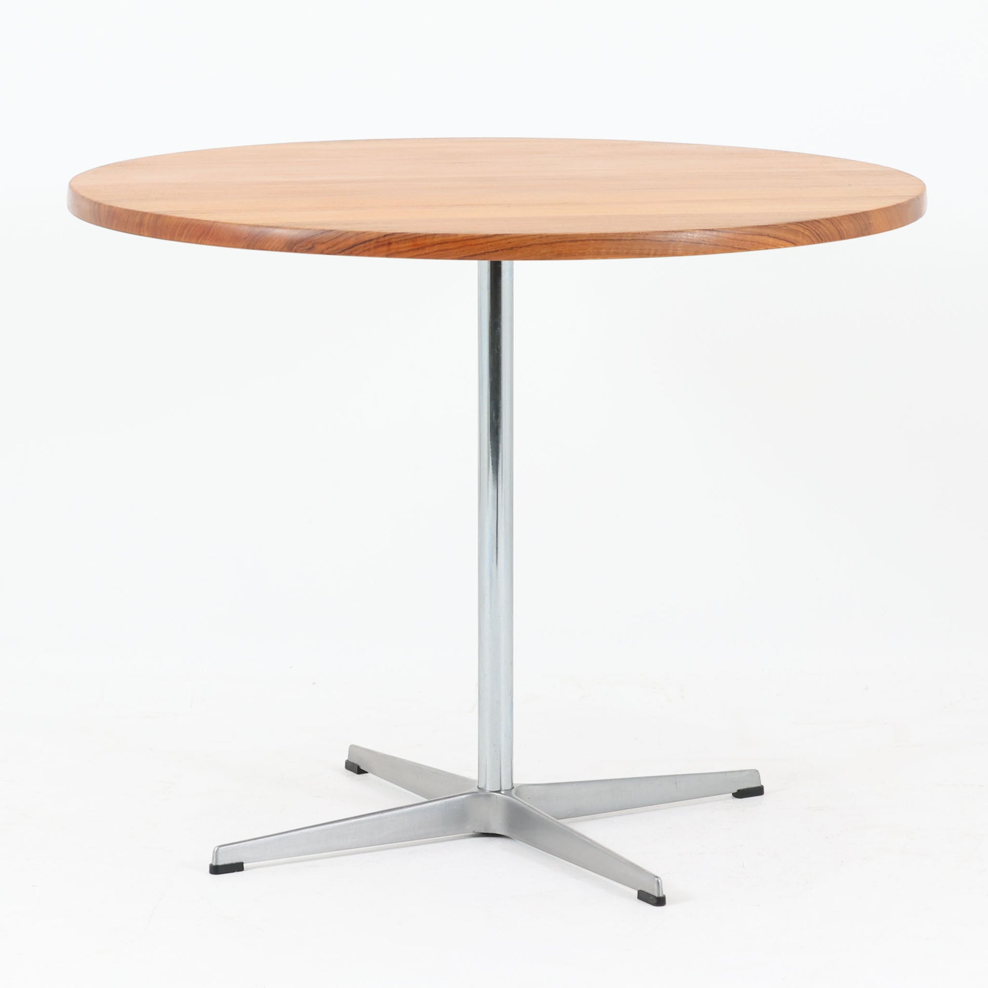 Arne Jacobsenがデザインし、Fritz Hansenが製作した円形ダイニングテーブルです。直径90cmのチーク無垢天板は、豊かな木目と滑らかな円形フォルムが美しく、空間に柔らかな印象をもたらします。シャープなスチール製の一本脚と4本スポークベースが軽快で洗練された佇まいを生み、ヤコブセンらしい機能美が際立つ一台。2～4人で使いやすいサイズ感で、ダイニングテーブルとしてはもちろん、カフェテーブルやラウンジ空間での打ち合わせ用テーブルとしてもおすすめです。中でもチーク無垢材仕様の個体は流通数が少なく珍しく、北欧ビンテージ市場でも希少性の高いモデルとして魅力を放ちます。経年により深みを増した木肌と無駄のない構造が、空間に上質な存在感を添えてくれます。